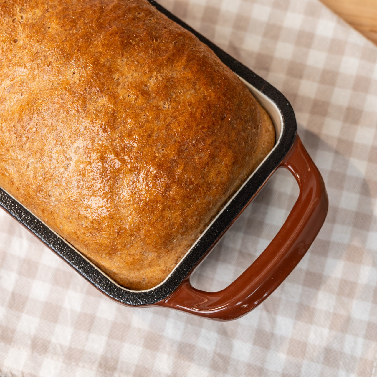 Loaf of bread in a brown baking dish on a checkered tablecloth