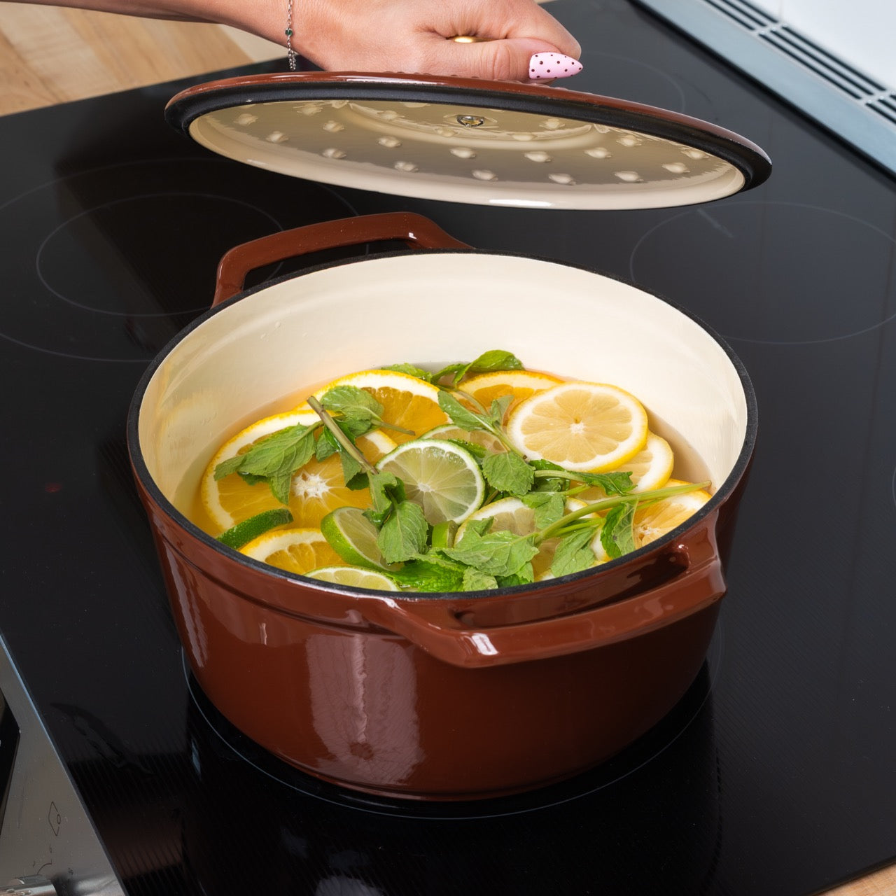 Brown pot on a stove with lemons and herbs inside, lid open