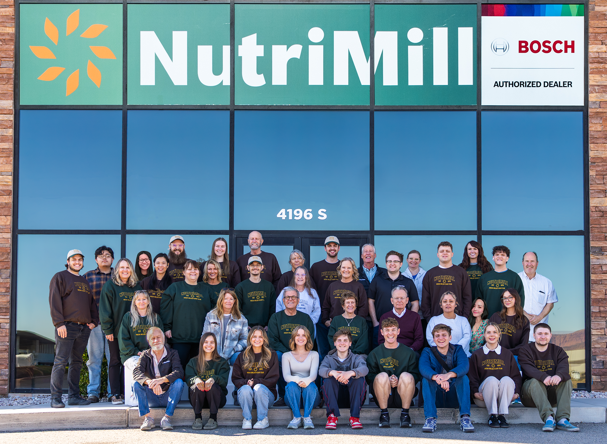The NutriMill team posed together in NutriMill sweatshirts in front of the NutriMill and Bosch Authorized Dealer building