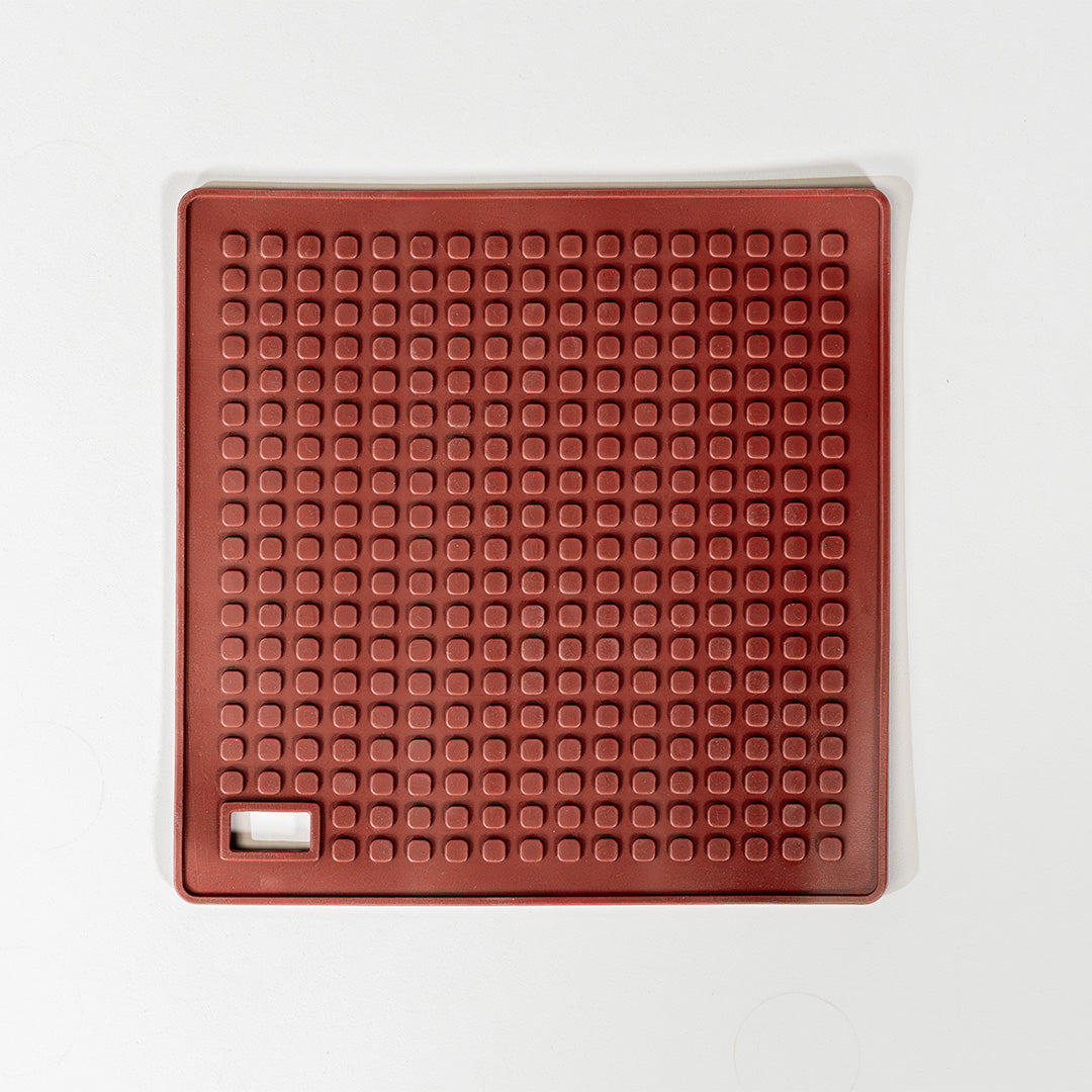 A red silicone hot pot holder with a textured surface and a handle.