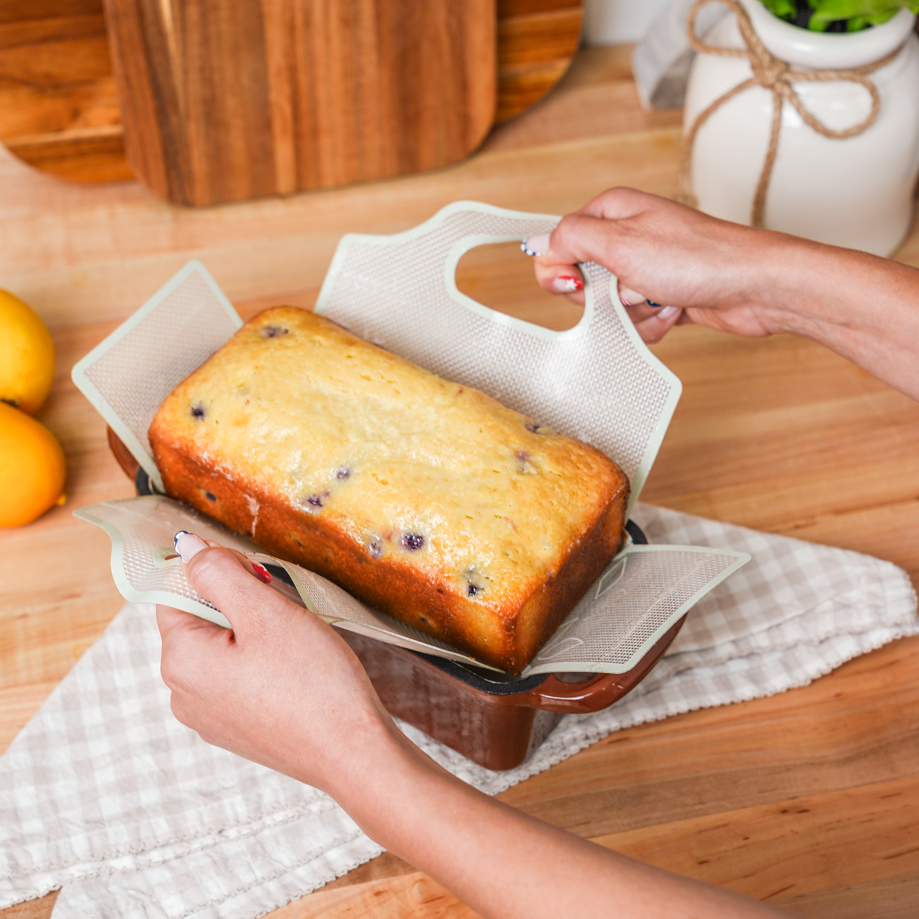 Hands lifting a blueberry lemon loaf from a bread pan using a silicone baking sling