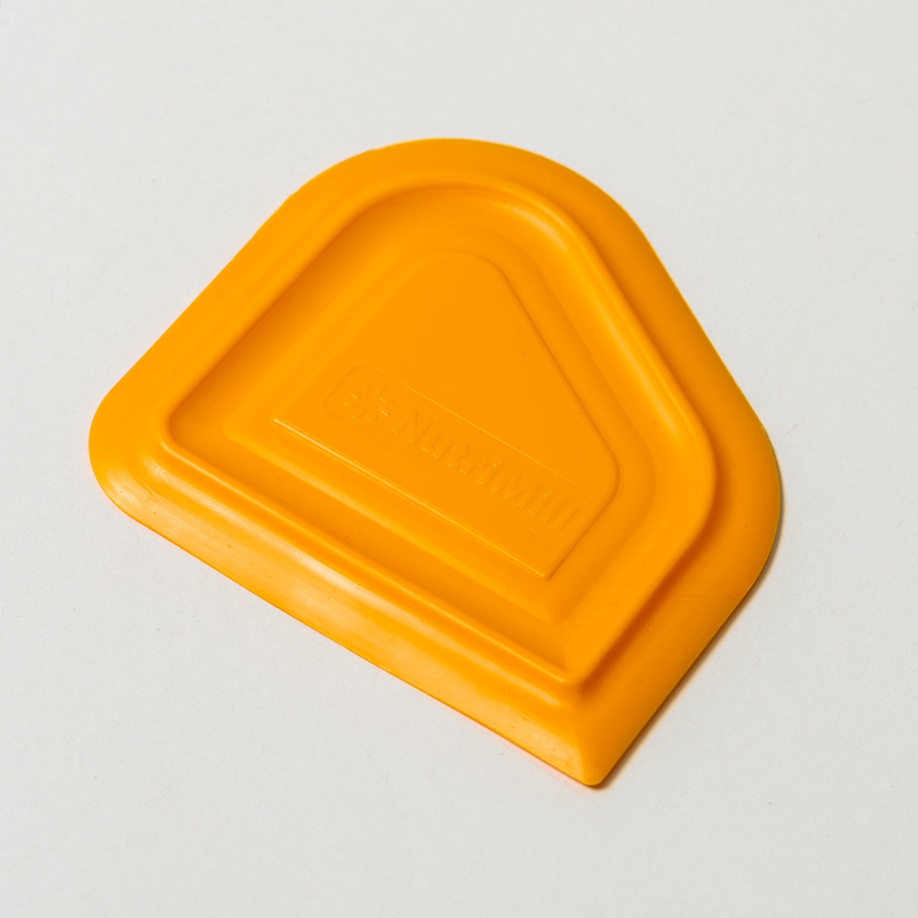 Top angled view of a NutriMill orange easy scrape bowl scraper on a white background