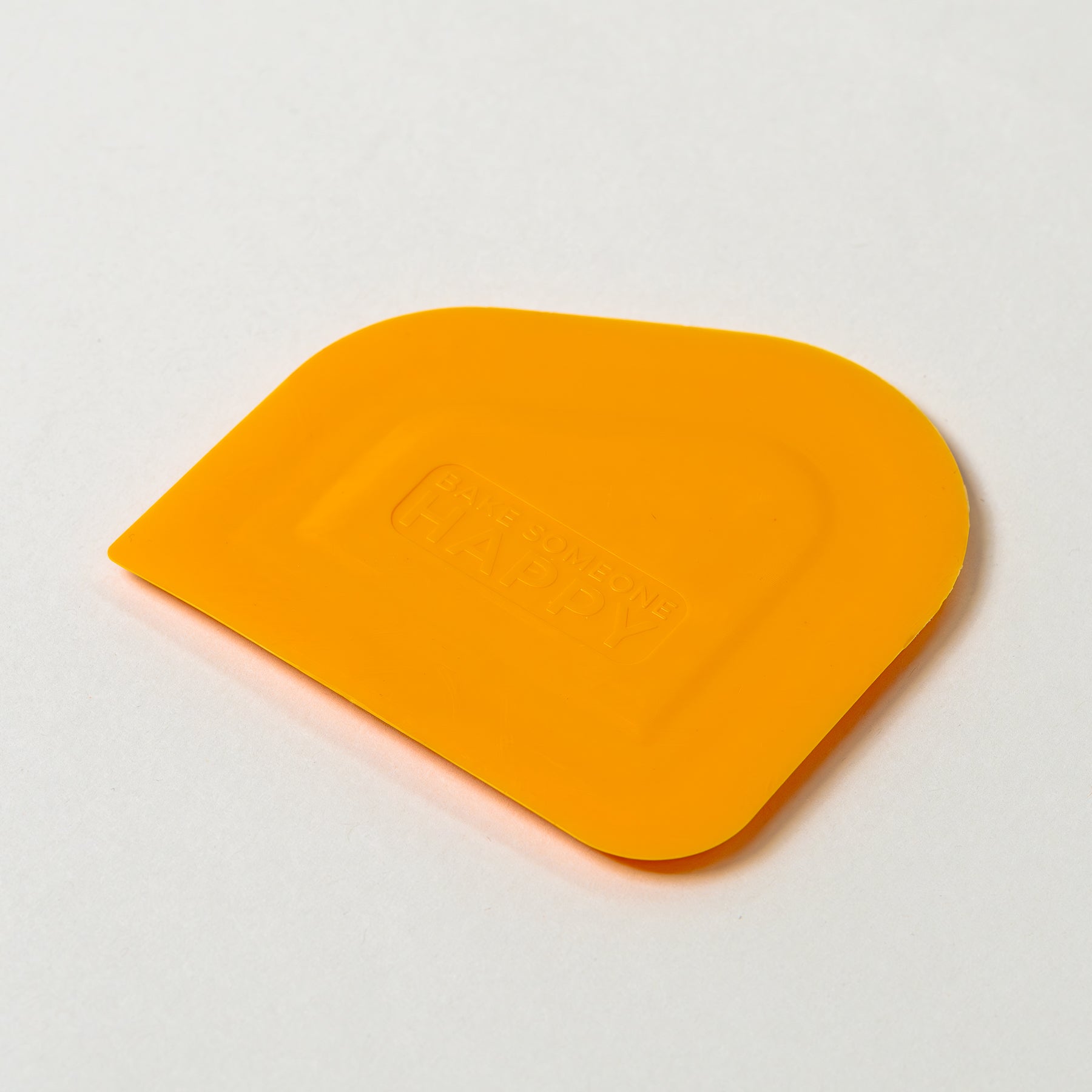NutriMill orange easy scrape bowl scraper with 'Bake someone happy' embossed on a white background