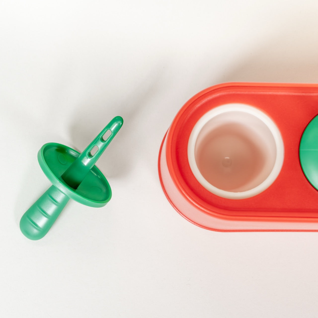 Green popsicle stick and red container with white silicone inside the mold on a light background