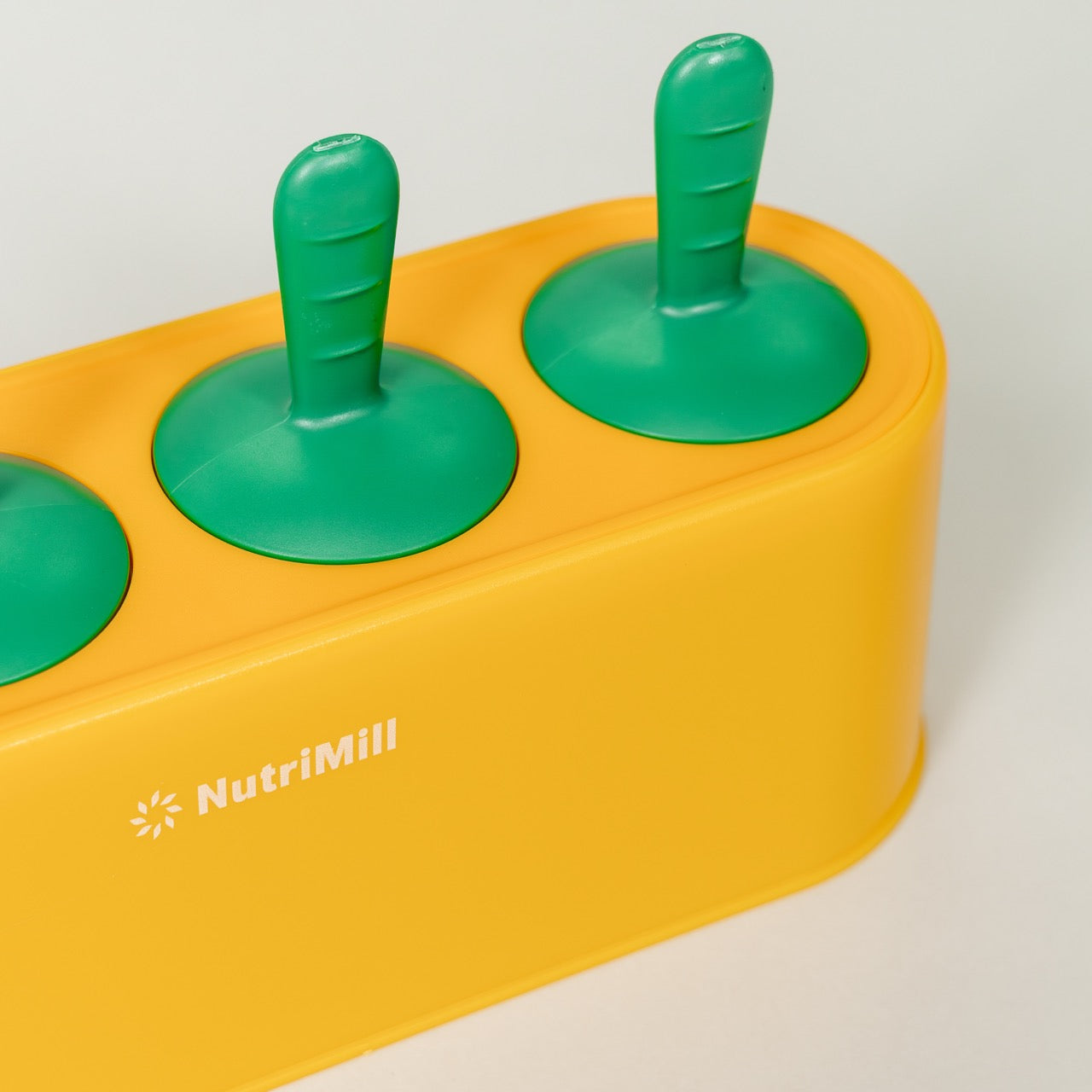 Yellow popsicle mold with green handles on a white background