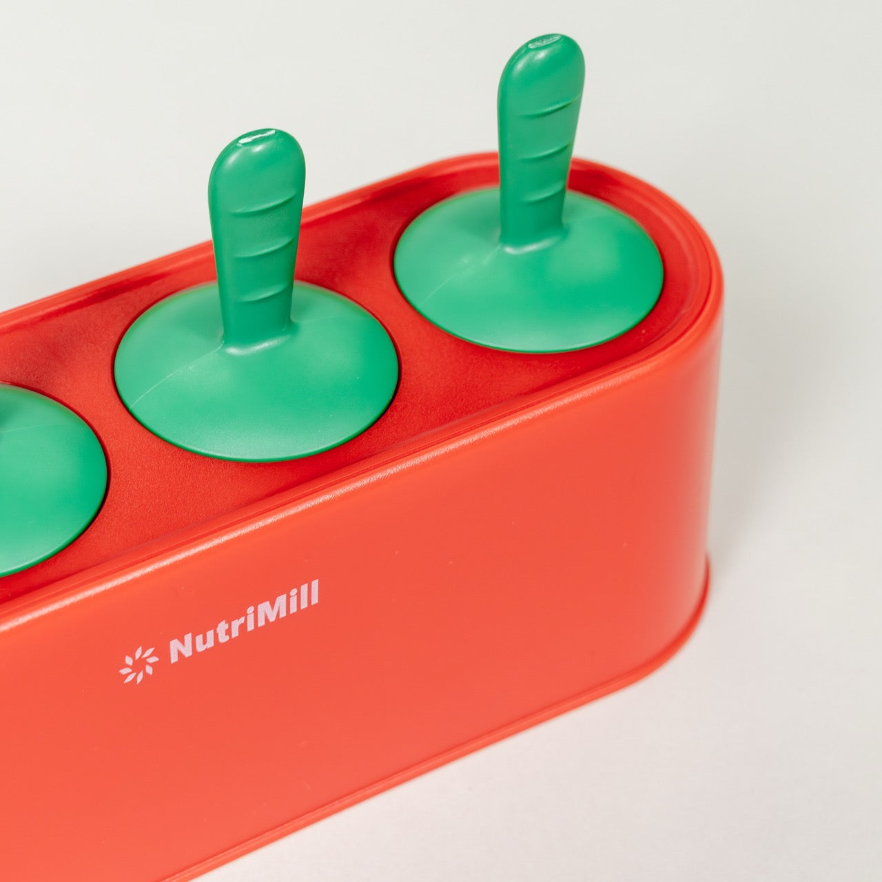 Red popsicle mold with green handles on a white background, featuring the NutriMill brand.