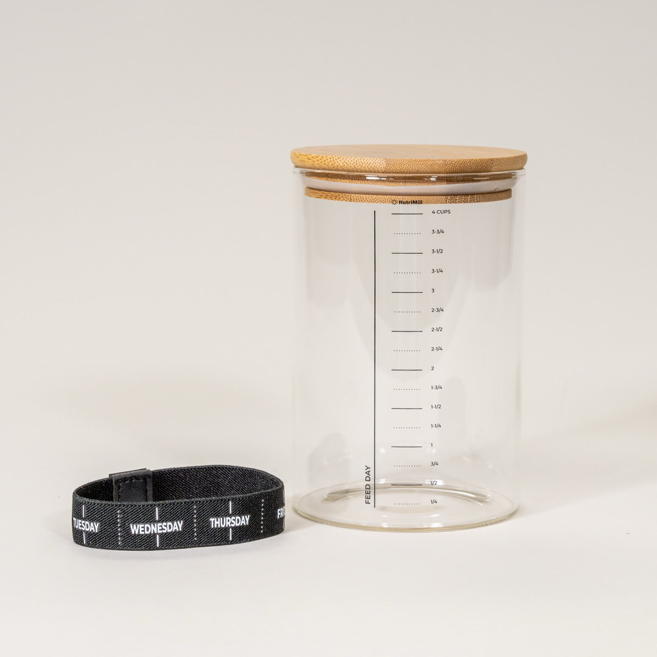 A clear glass sourdough starter jar with measurement markings, accompanied by a bamboo lid and a black day marker band.