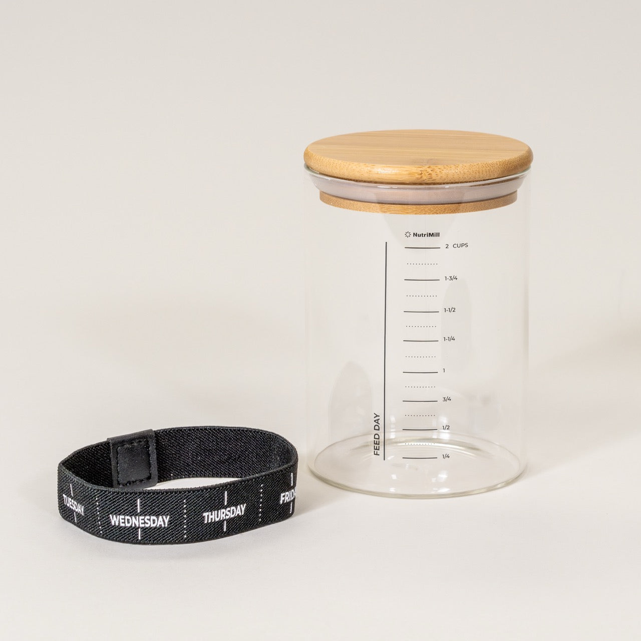 A clear glass pint jar with measurement markings, accompanied by a bamboo lid and a black adjustable day marker band.