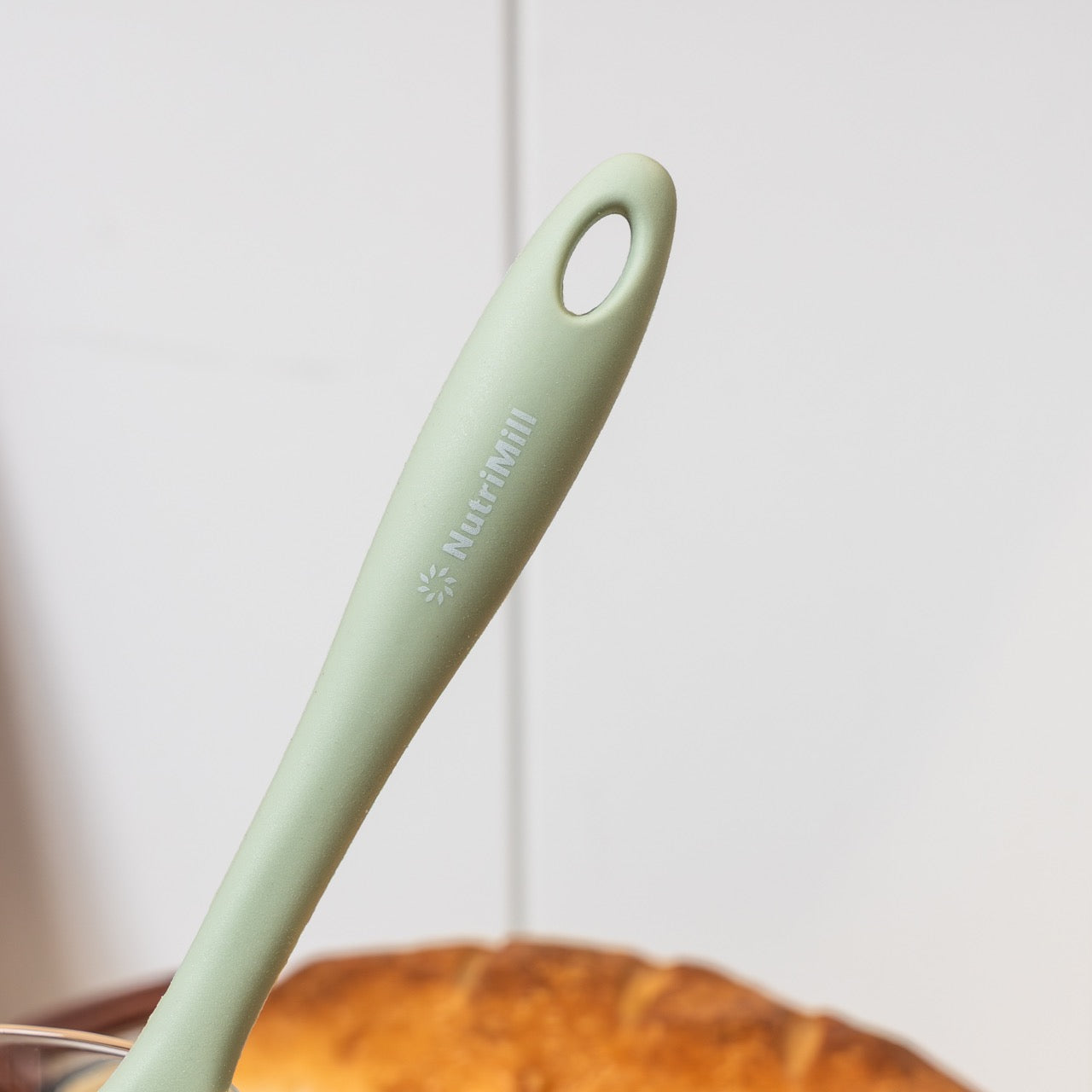 Light green silicone scraper handle with a NutriMill Logo