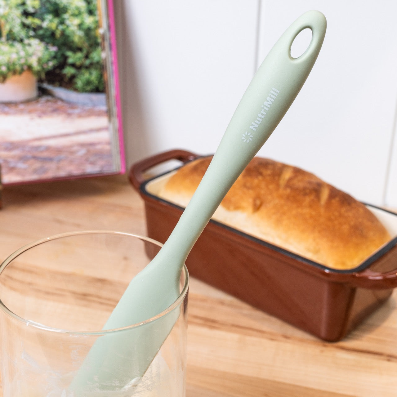 Silicone spatula in a glass sourdough jar with bread in the background