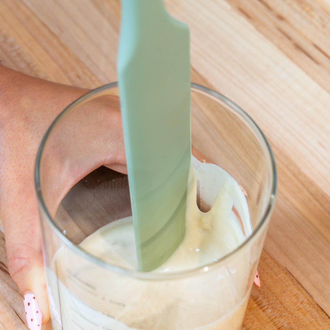 Glass of sourdough starter with a green spatula scraping the sides.