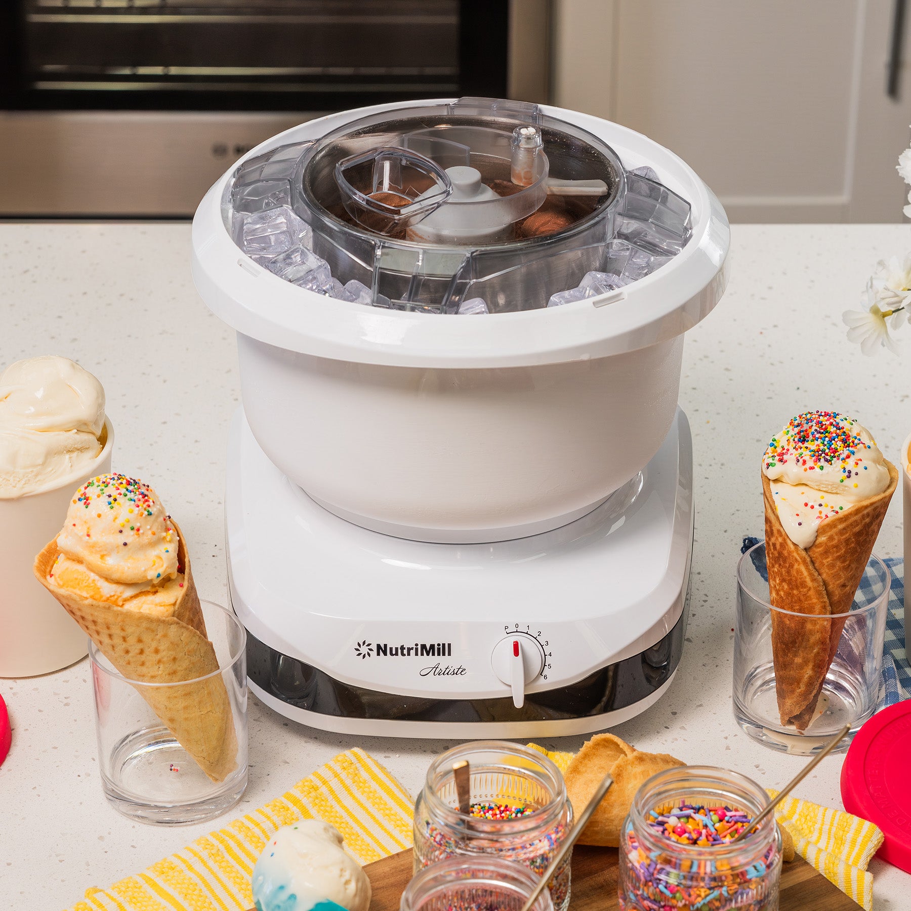 White ice cream maker on a counter surrounded by ice cream cones and dishes