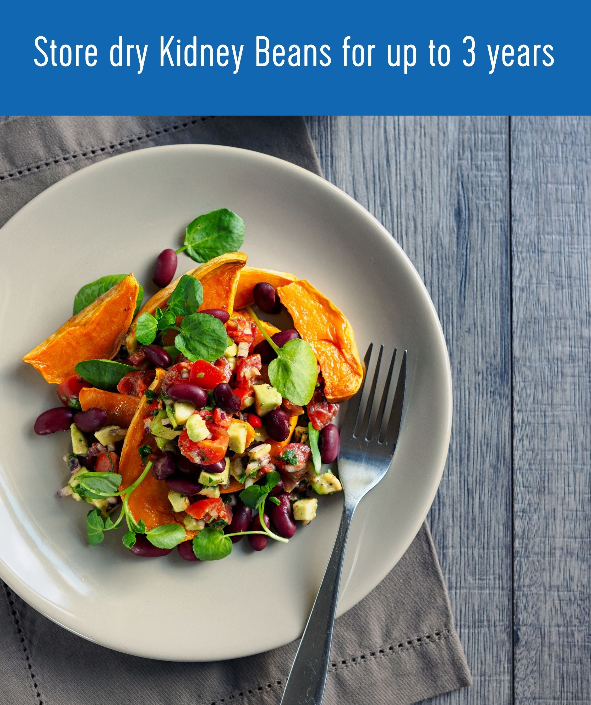 Plate of kidney bean salad with sweet potato, avocado, tomato, and watercress with a fork on a grey napkin and wood surface, with text 'Store dry Kidney Beans for up to 3 years'