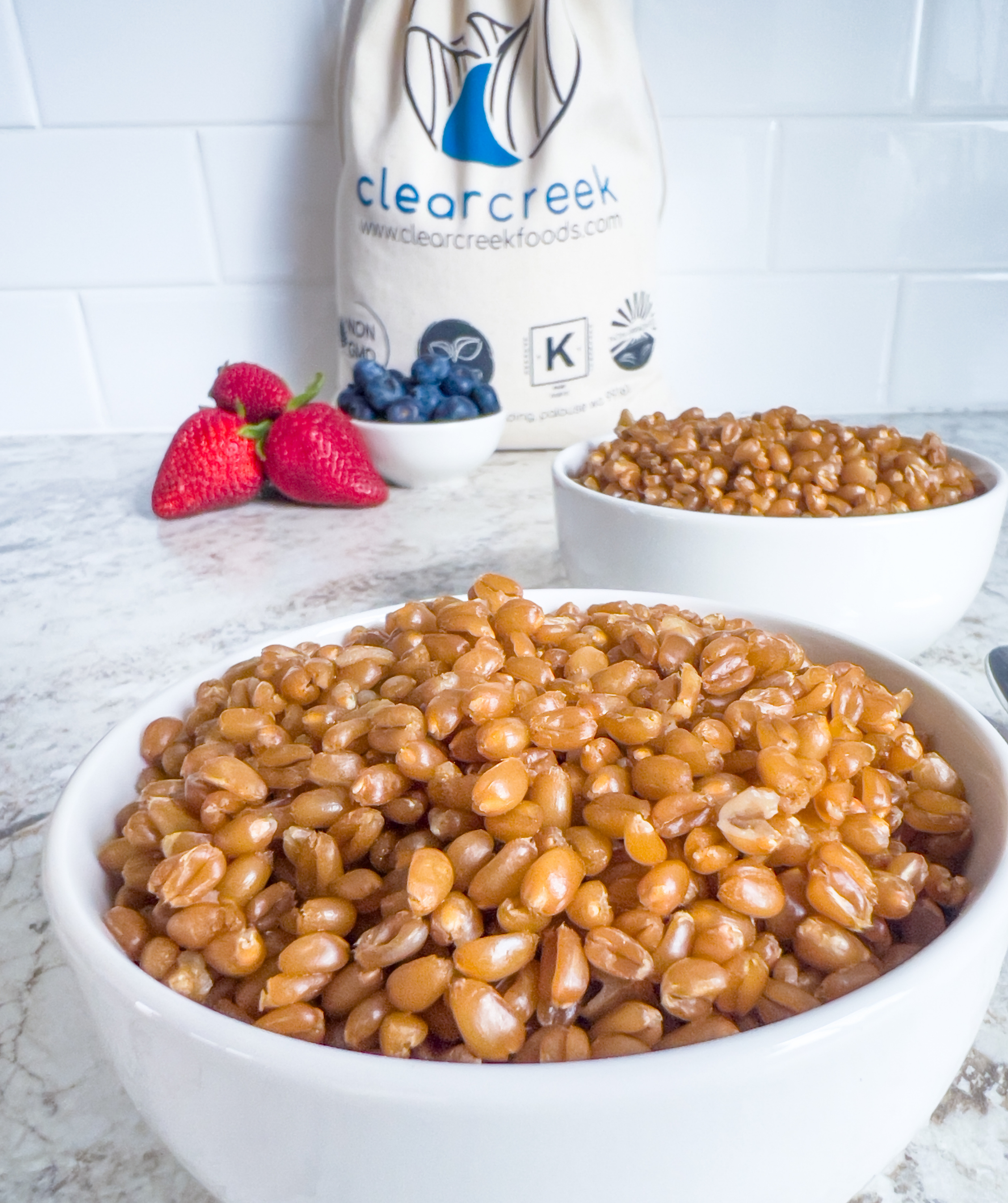 Clear Creek lifestyle photo of bowls of cooked wheat berries with fresh strawberries and blueberries and a branded canvas bag
