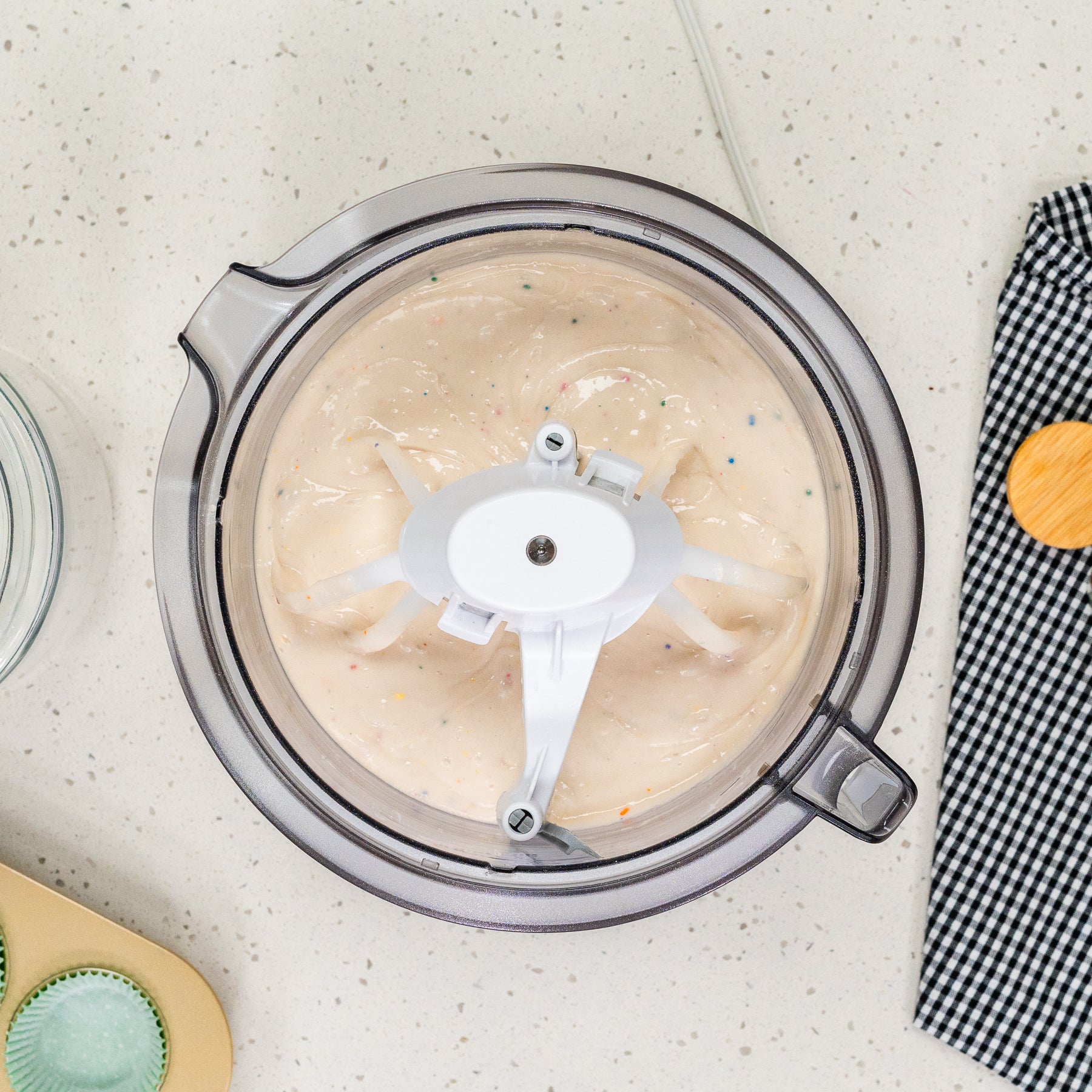 Bird's eye view of white batter with sprinkles in white bowl with white attachment sitting on a white speckled counter