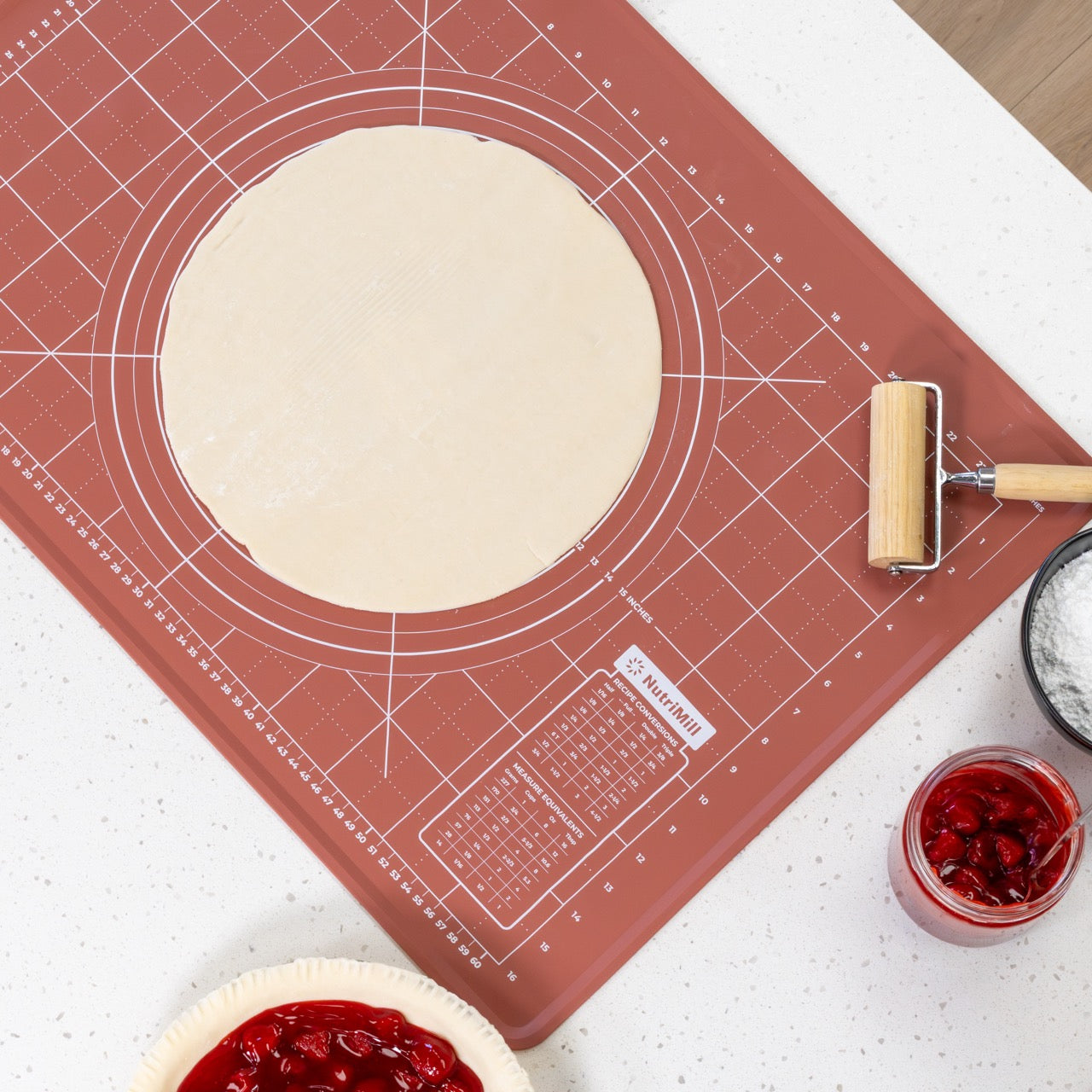 Baking mat with pie crust and rolling tool on a kitchen counter.