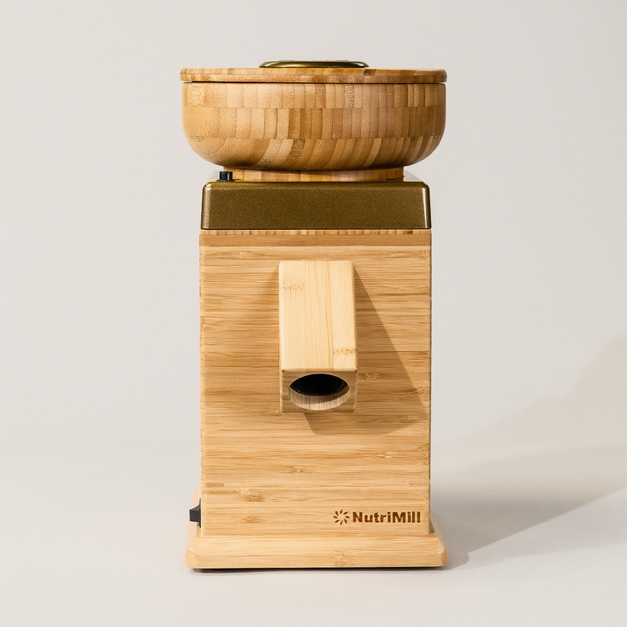 A gold NutriMill Harvest grain mill made of bamboo with a bowl on top and a knob in the front, displaying the brand name.