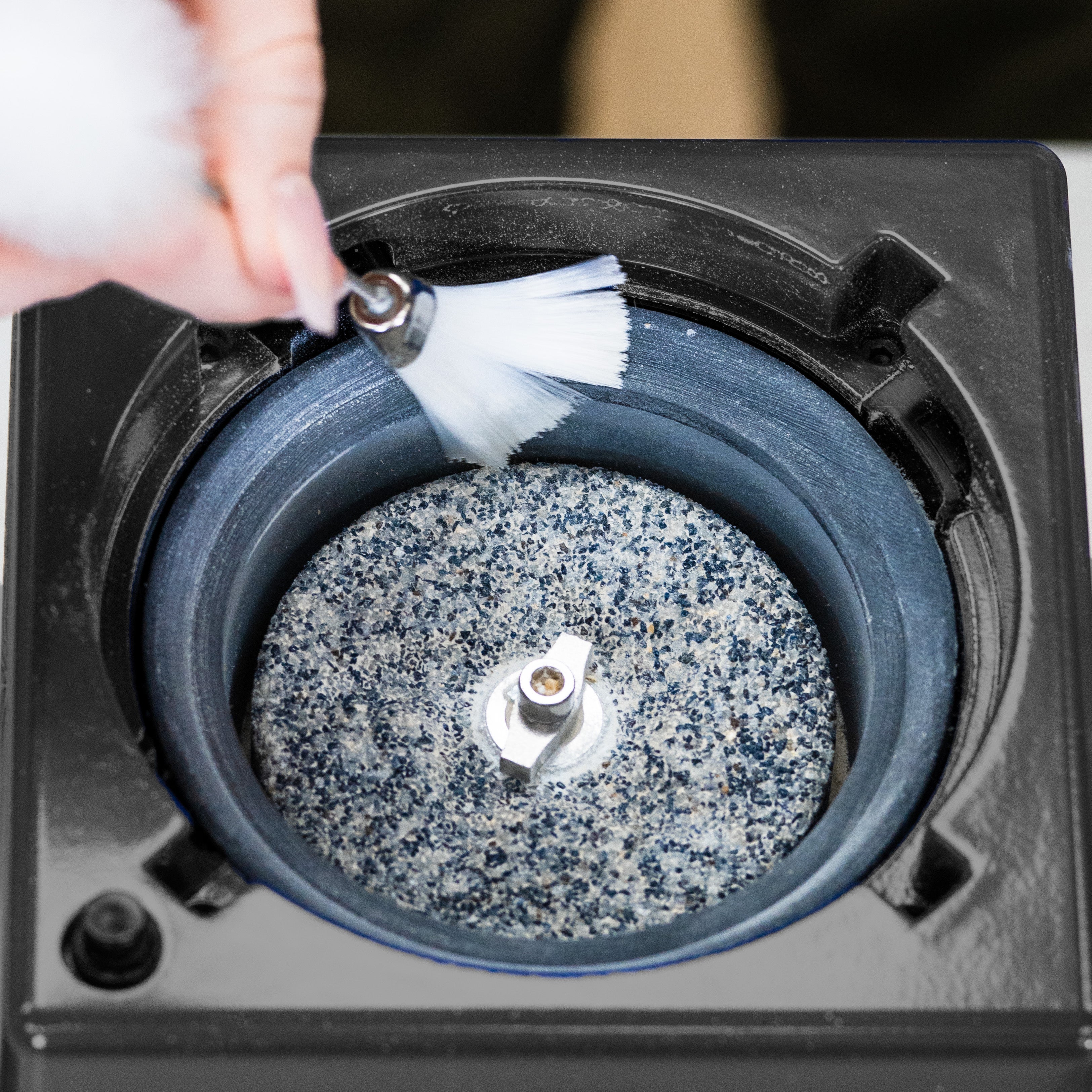 Cleaning a round stone with a white soft brush that is inside of a black-trimmed NutriMill harvest grain mill