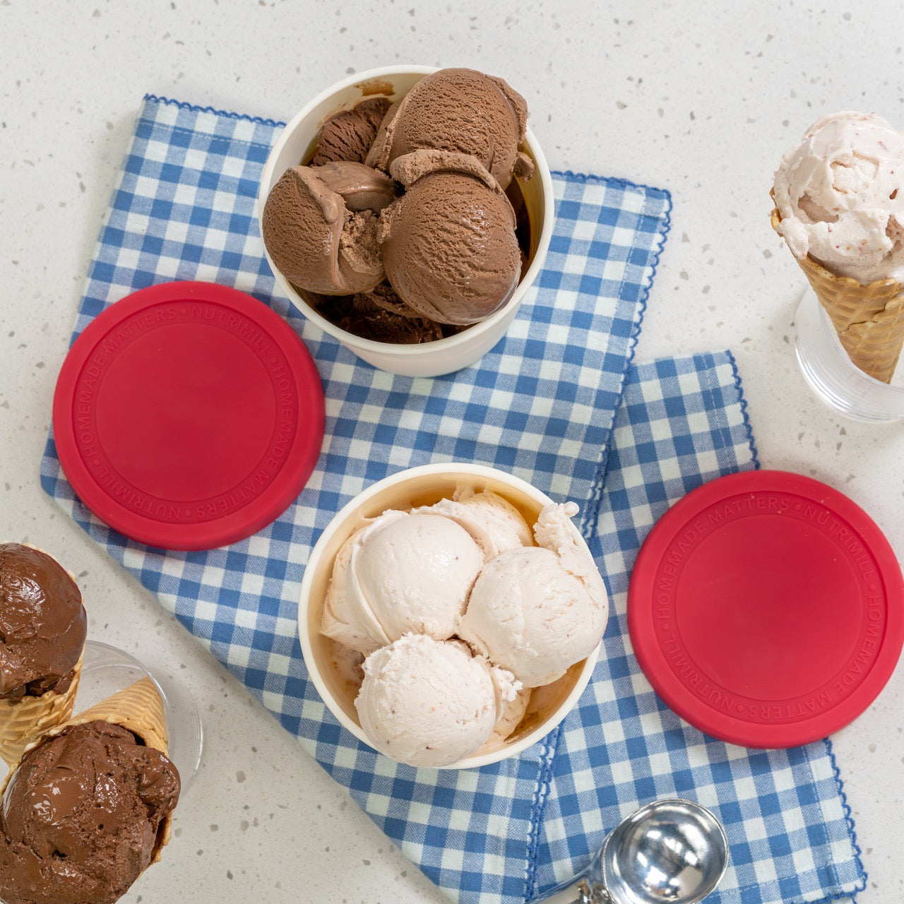 Two containers of ice cream with red lids on a blue checkered cloth.