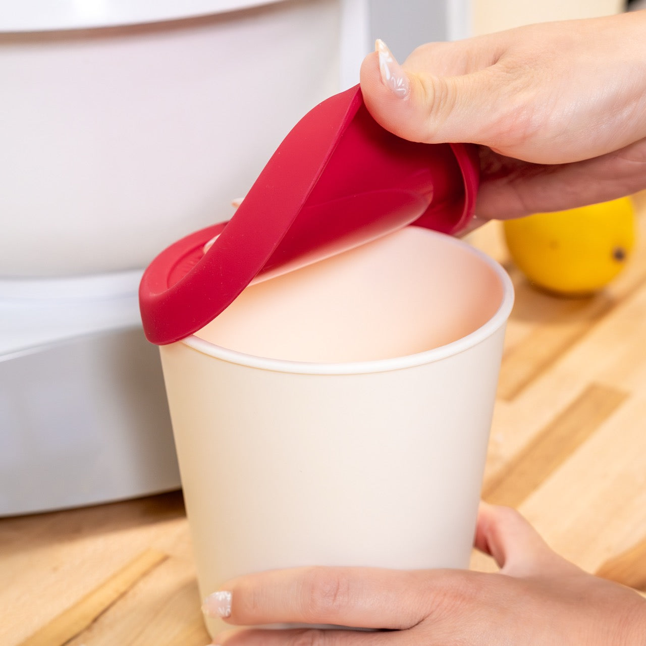 A person is opening a white ice cream container on a wooden surface.