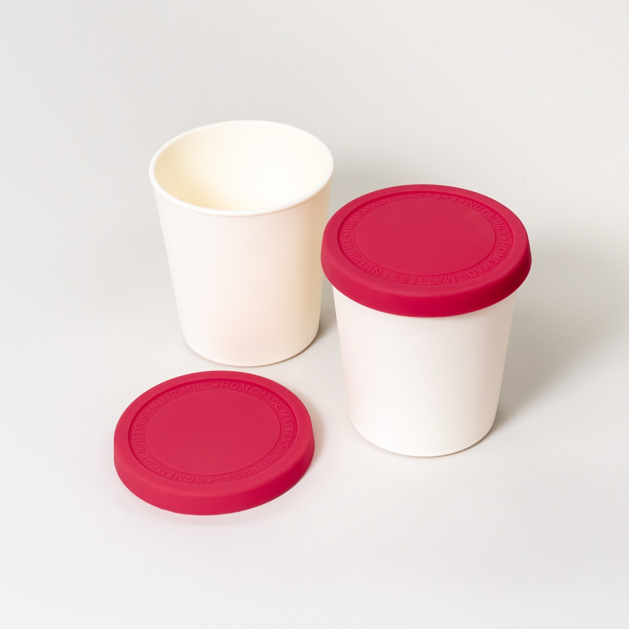 Two white reusable containers with red lids on a light gray background