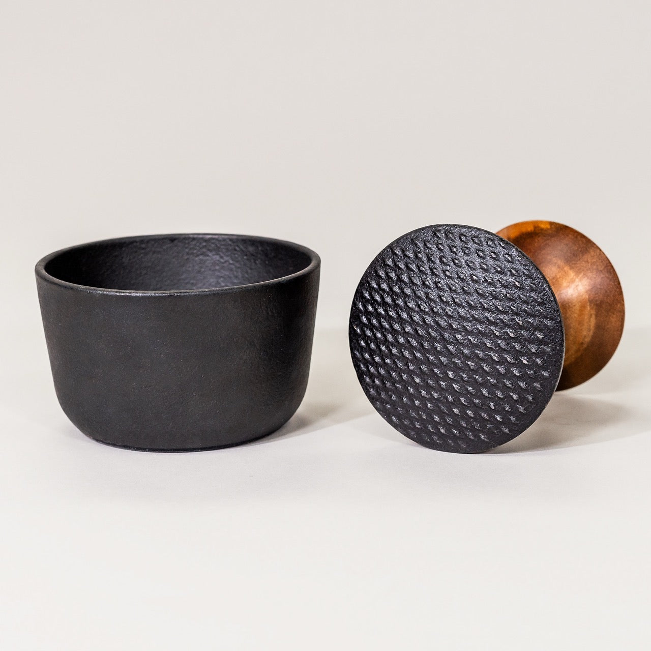 A black cast iron mortar with a pestle next to it, both on a white background.