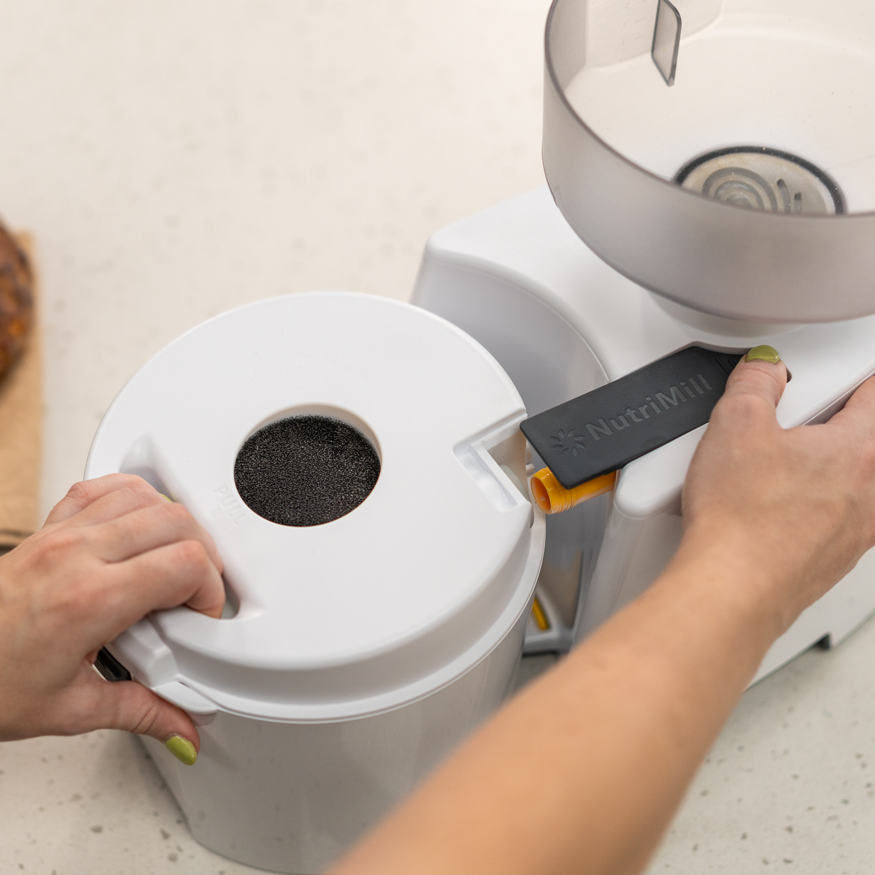 Person pulling flour canister off of the impact grain mill on a kitchen counter.