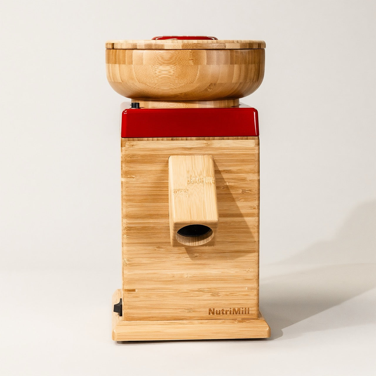 A NutriMill Harvest grain mill in red and bamboo wood colors, with a hopper on top and a base, displayed on a white background.