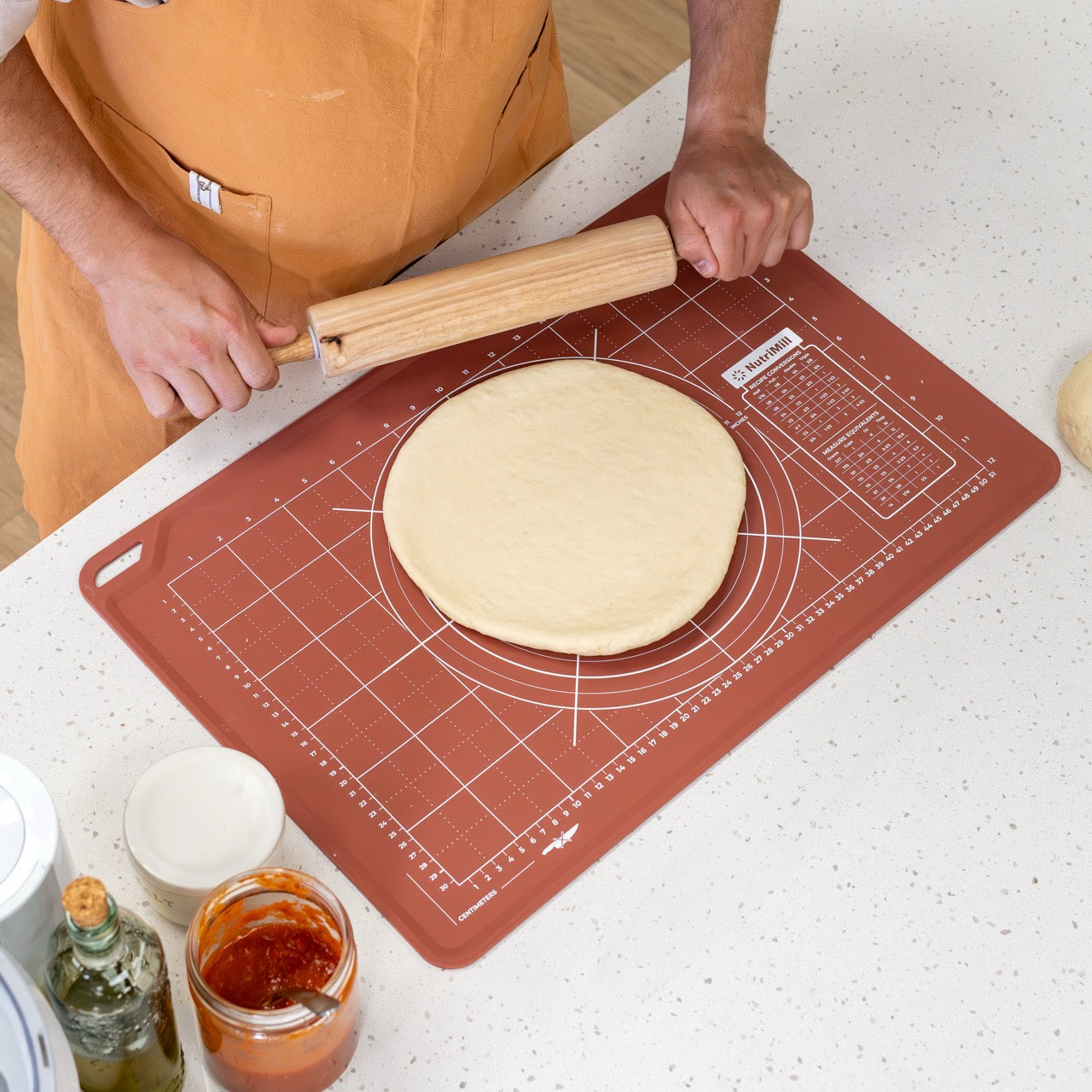 Person rolling dough on a silicone baking mat with a wooden rolling pin.