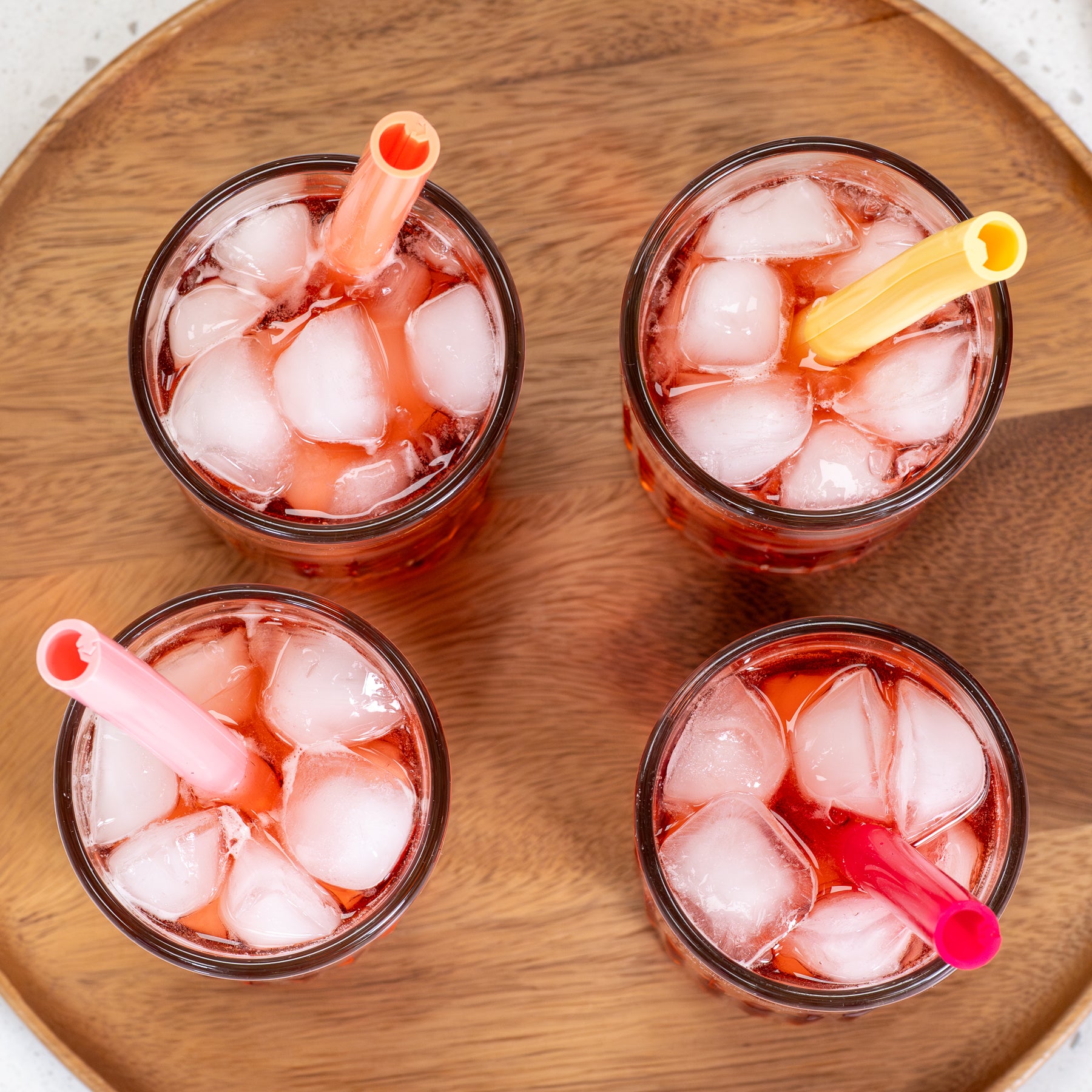 Four glasses of iced drinks with straws on a wooden tray.