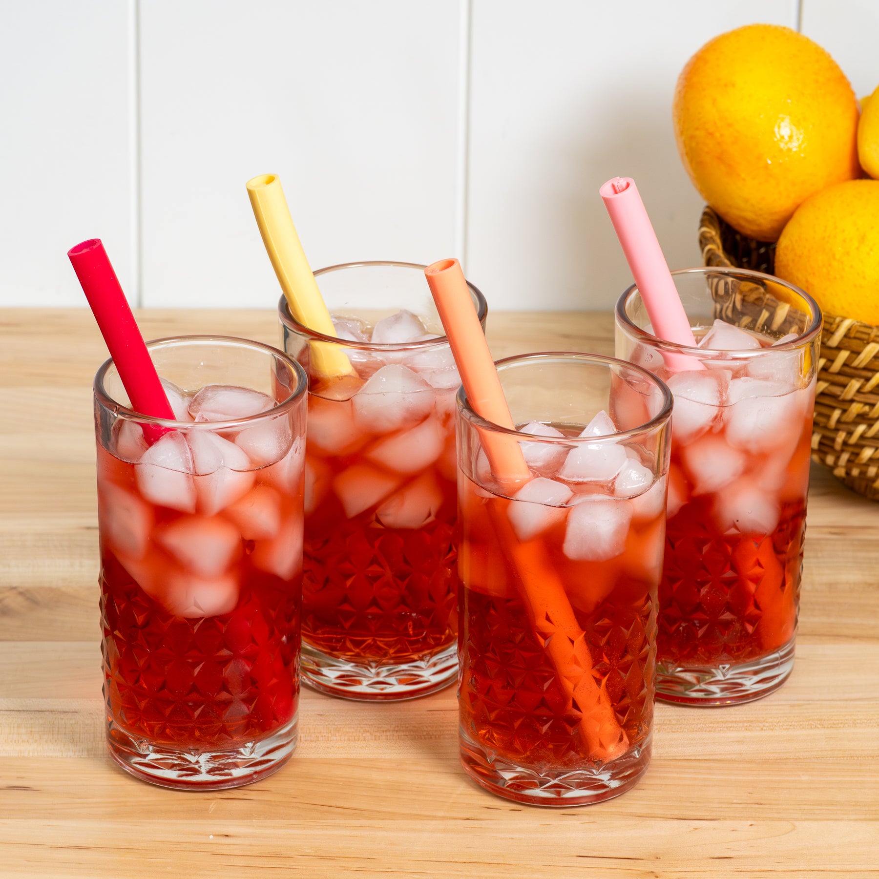 Four glasses of iced red drinks with straws on a wooden surface.