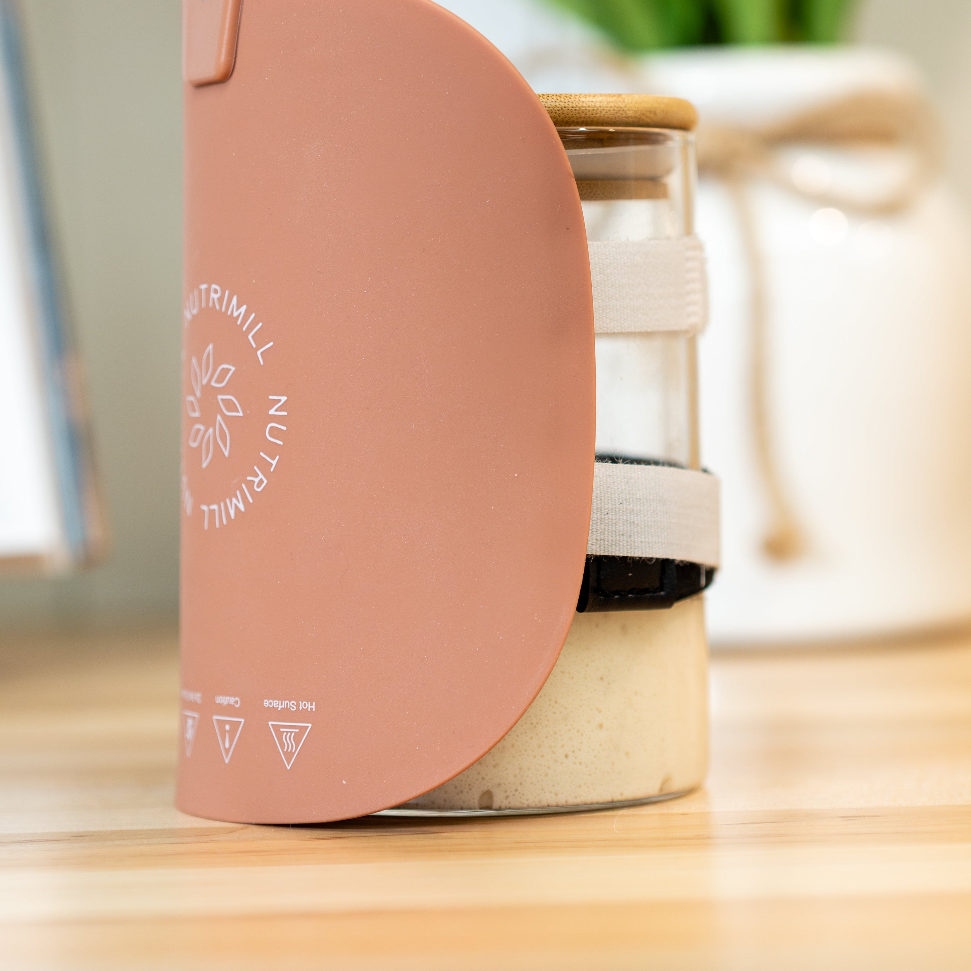 Terracotta-colored warming pad wrapped around sourdough starter jar on wooden counter