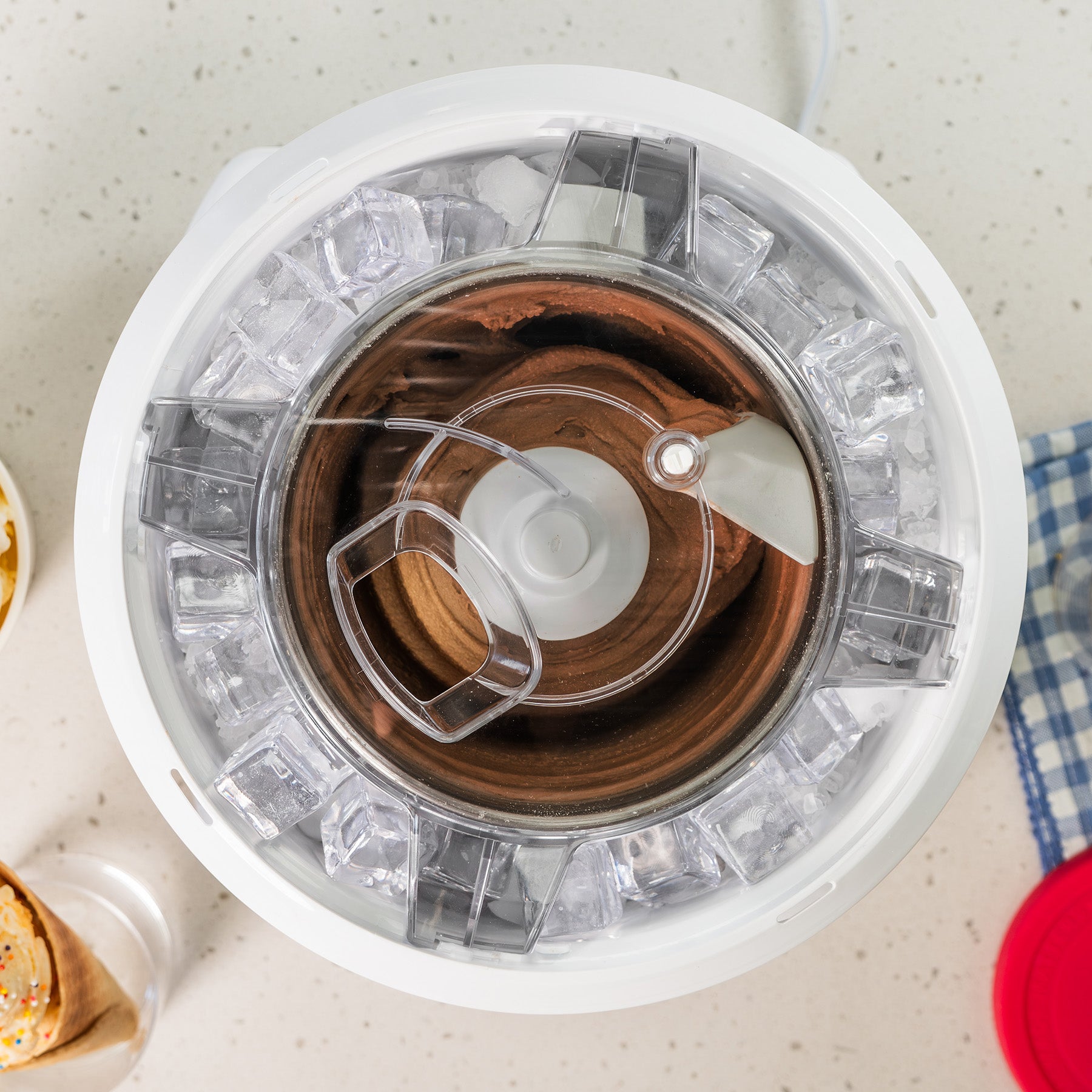 Top-down view of a white ice cream maker churning chocolate ice cream surrounded by ice