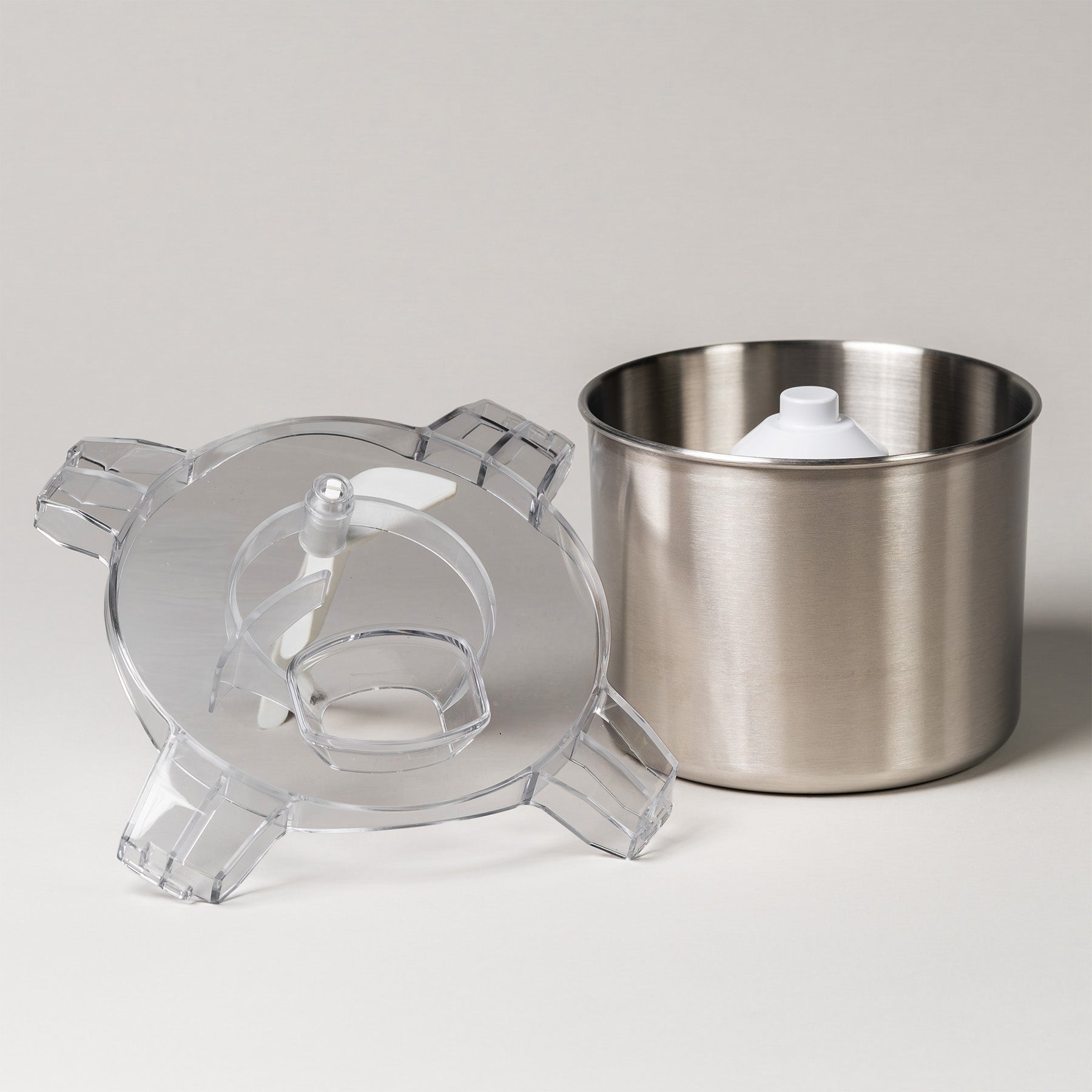White ice cream maker shown disassembled with its clear lid, paddle, and stainless steel bowl on a white background