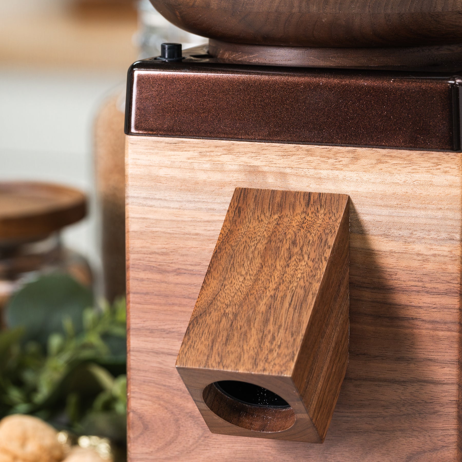 Walnut NutriMill Harvest grain mill with cocoa-colored trim on a blurred background