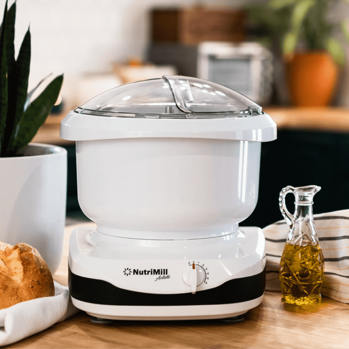 NutriMIll Artiste Kitchen stand mixer with black band on butcherblock countertop with fresh homemade bread.