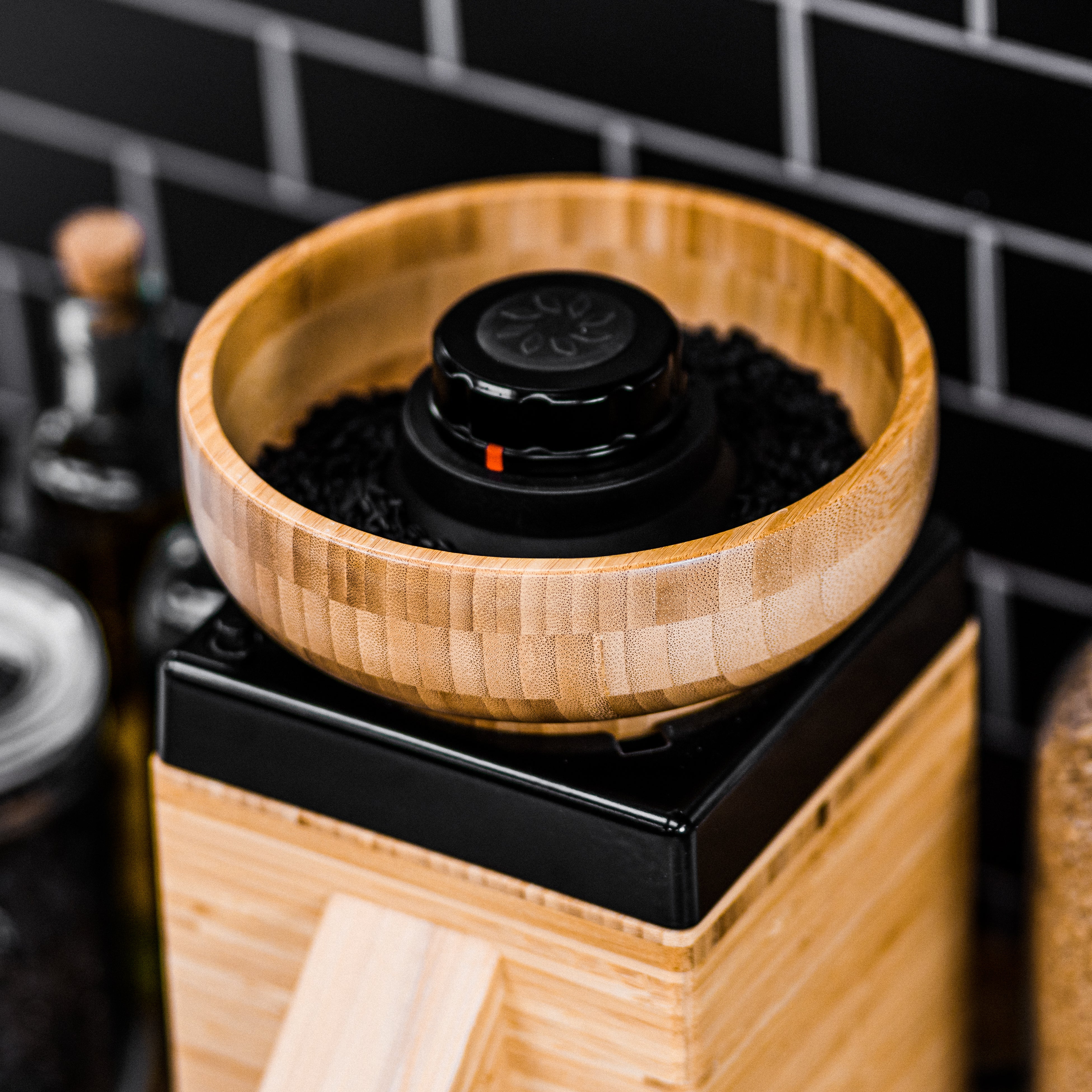 A countertop-sized bamboo flour mill with a black knob on the top, a wooden base, and a natural bamboo body.