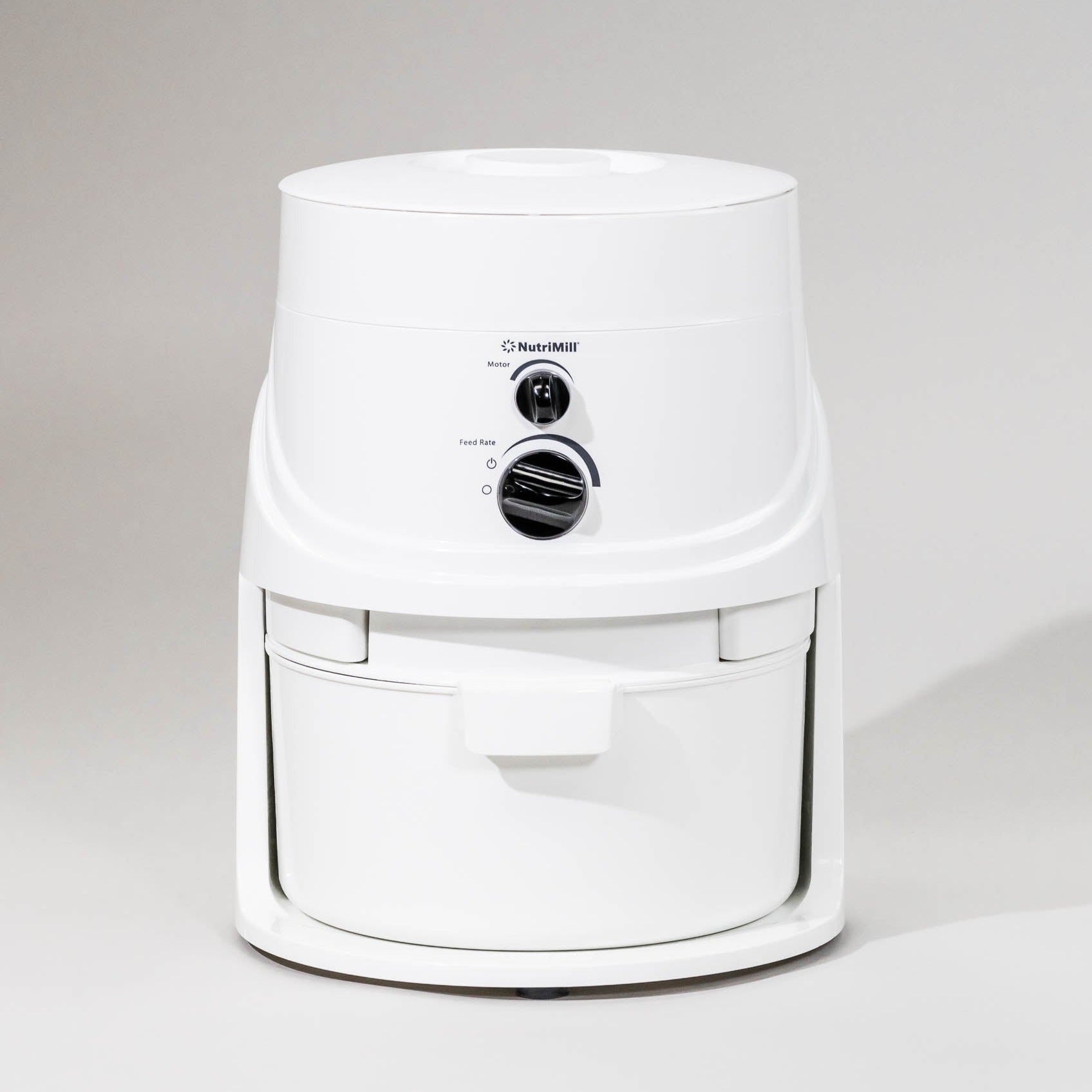 A white NutriMill Classic electric grain mill with a control knob on the front panel, set against a plain background.