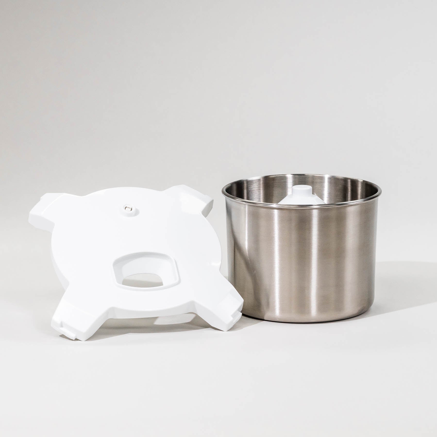 A stainless steel ice cream maker attachment with a white lid and churning paddle.