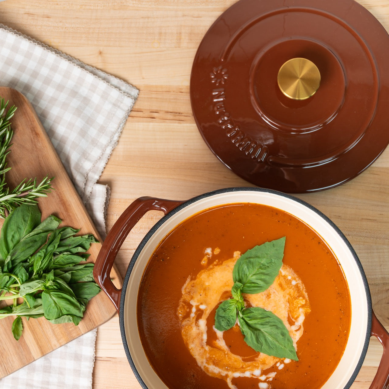 Brown ceramic pot with tomato soup and basil leaves on a wooden surface