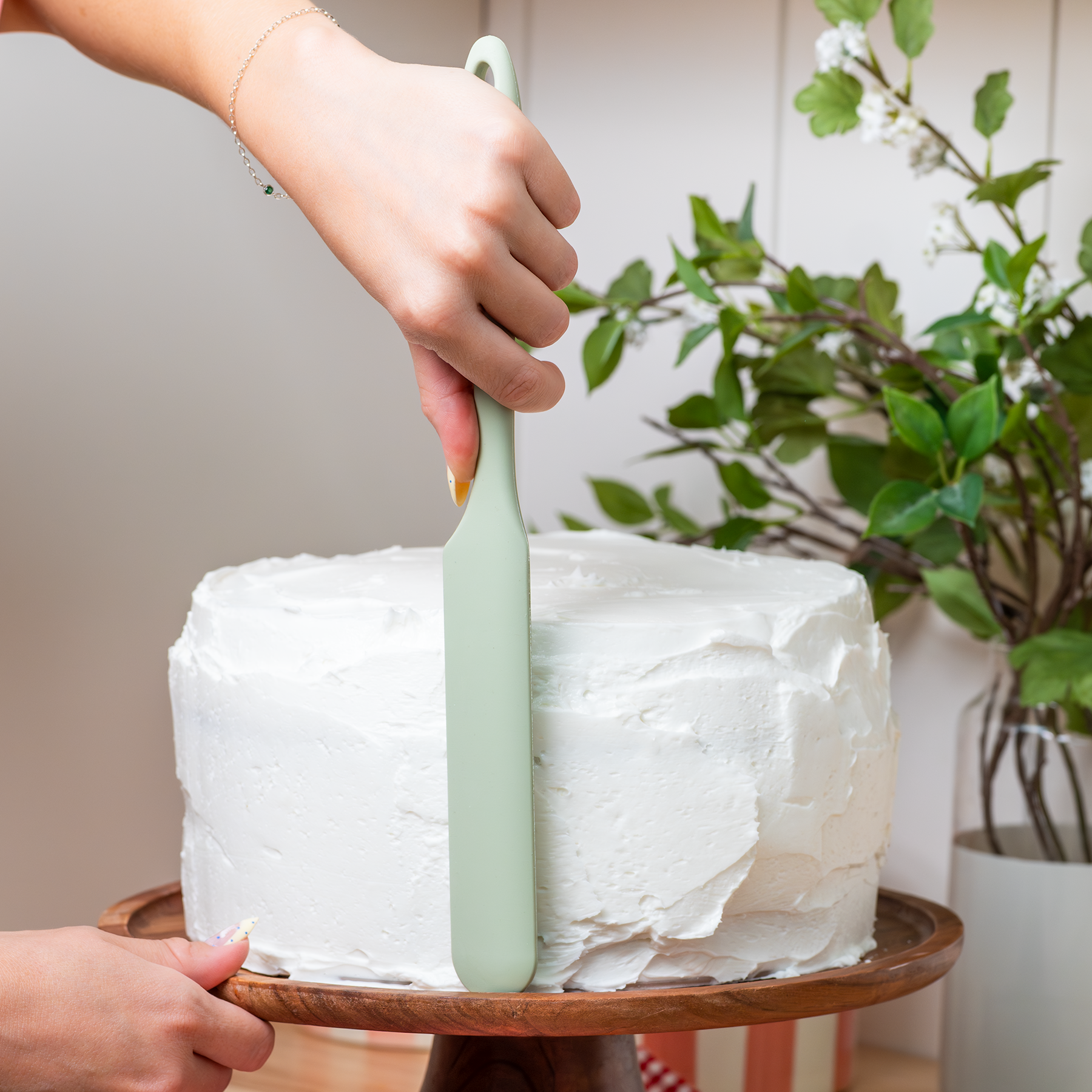 Person frosting a cake with a green spatula.