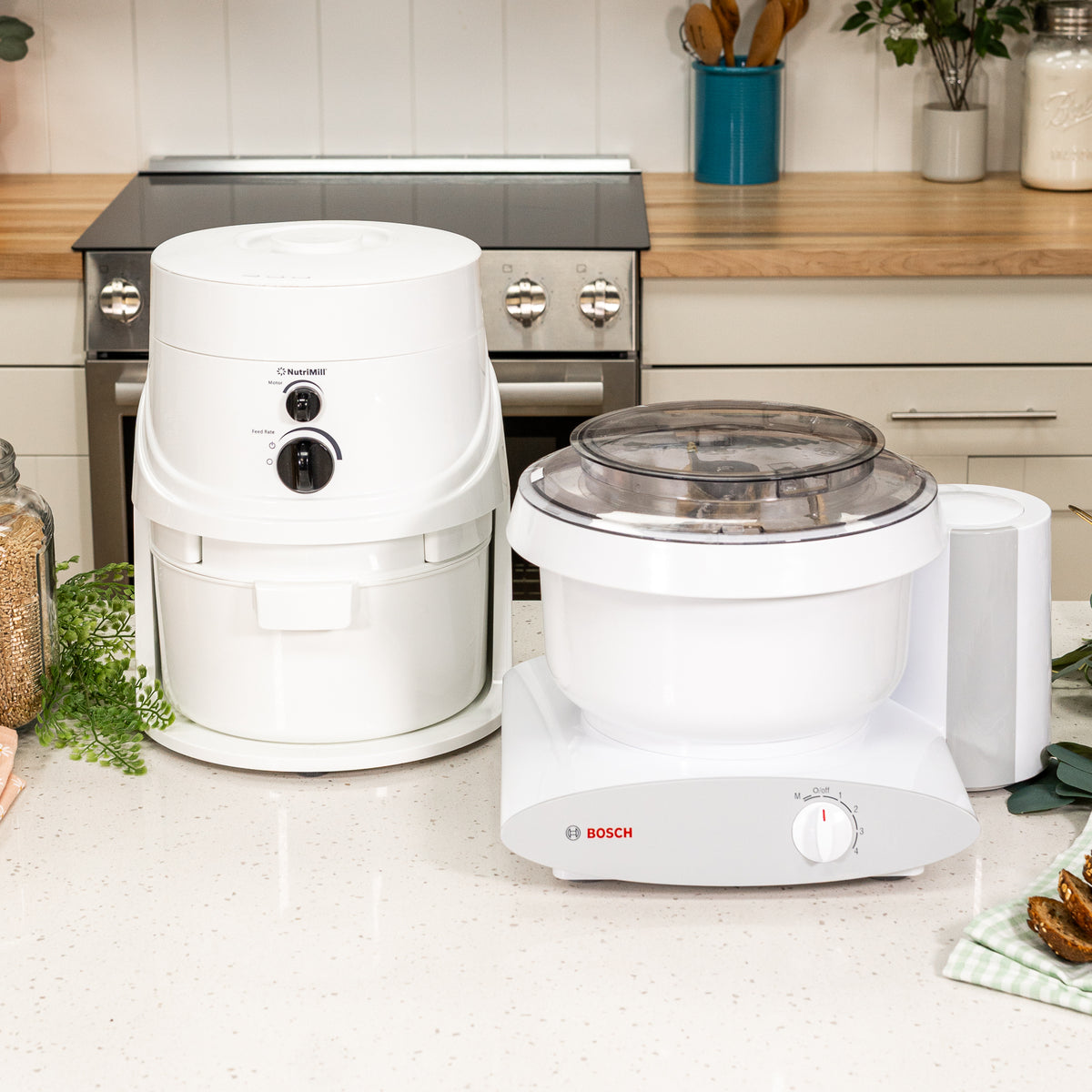 NutriMill classic grain mill and Bosch universal plus mixer next to each other on white speckled counter with kitchen in background