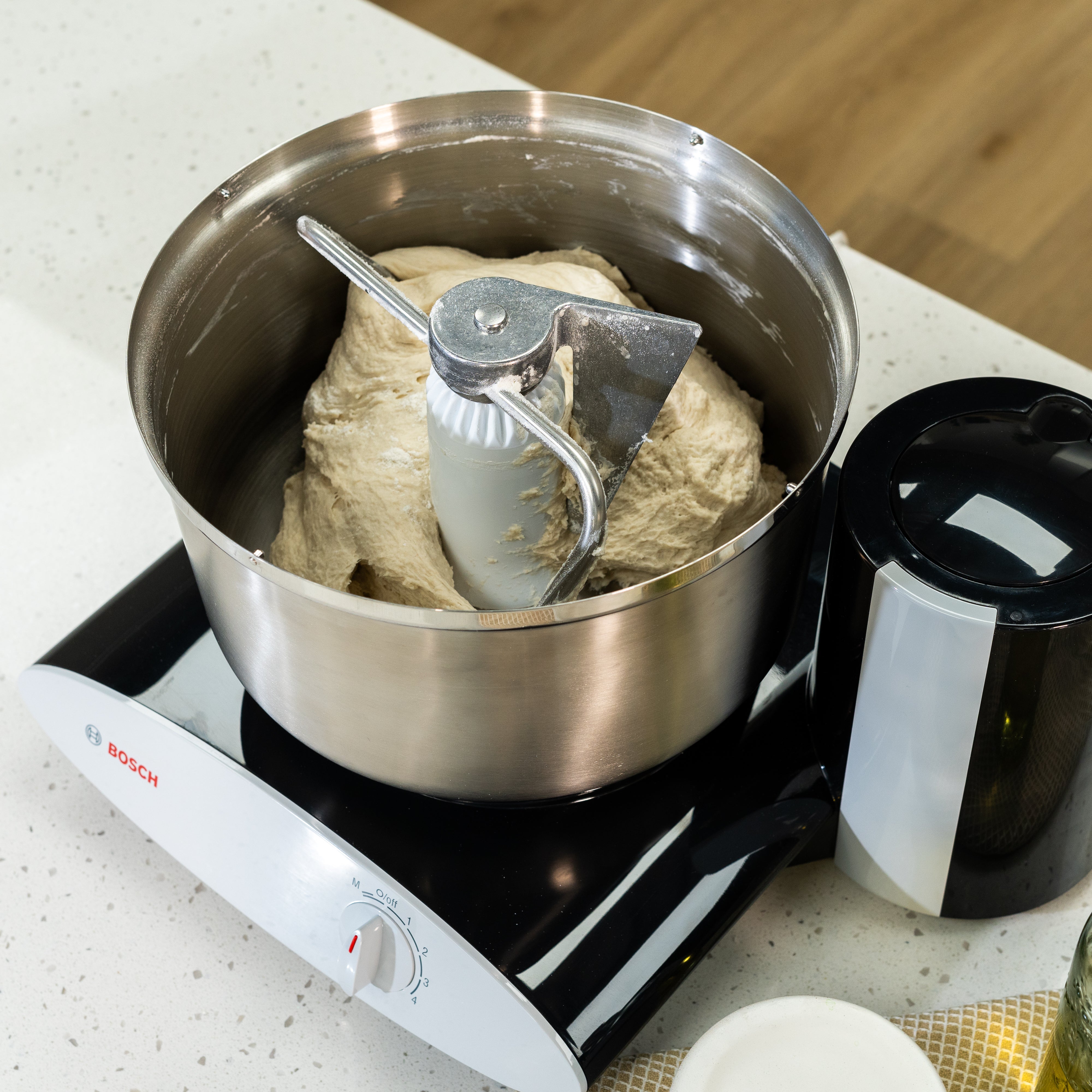 A black Bosch universal plus mixer mixing dough on a white kitchen counter