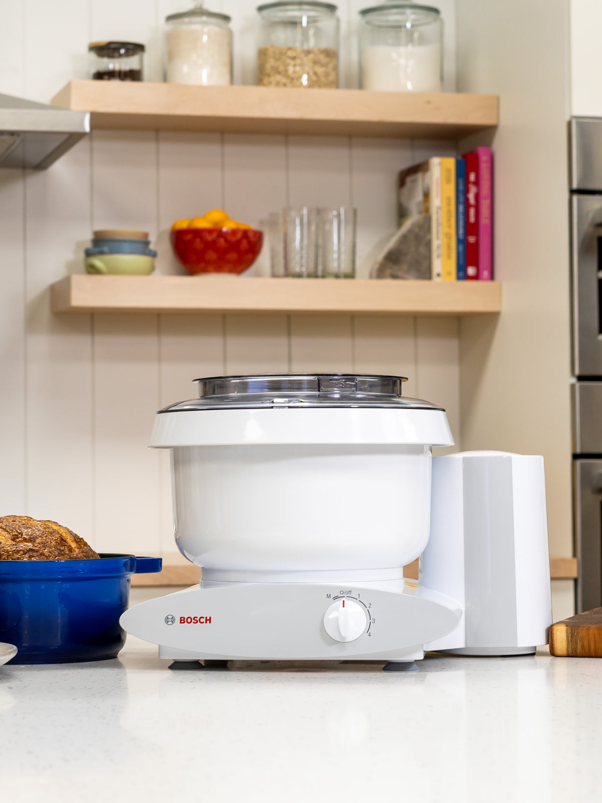 Bosch white universal plus mixer on a white kitchen counter next to a blue pot with bread inside