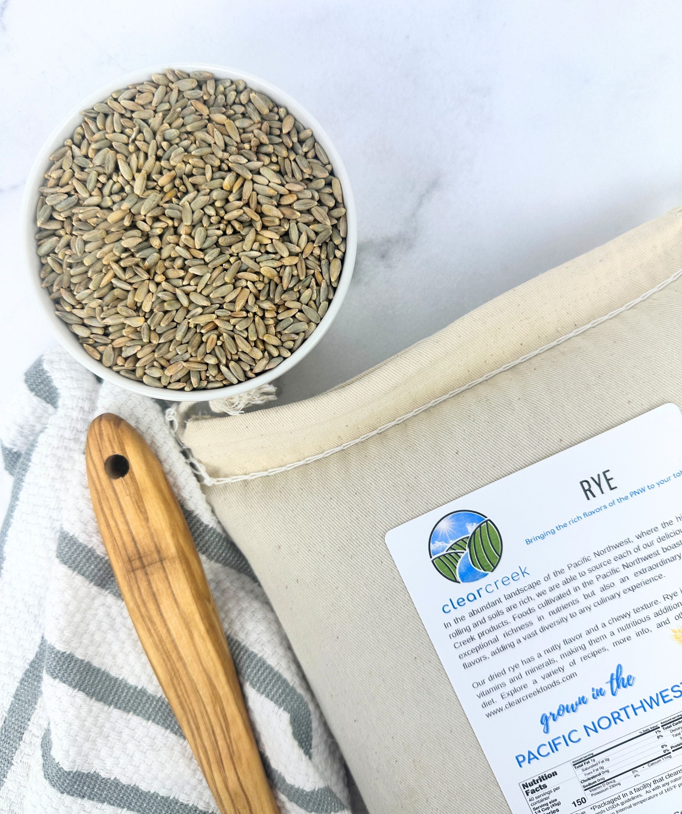 Clear Creek Rye canvas bag beside a bowl of rye berries with a wooden spoon