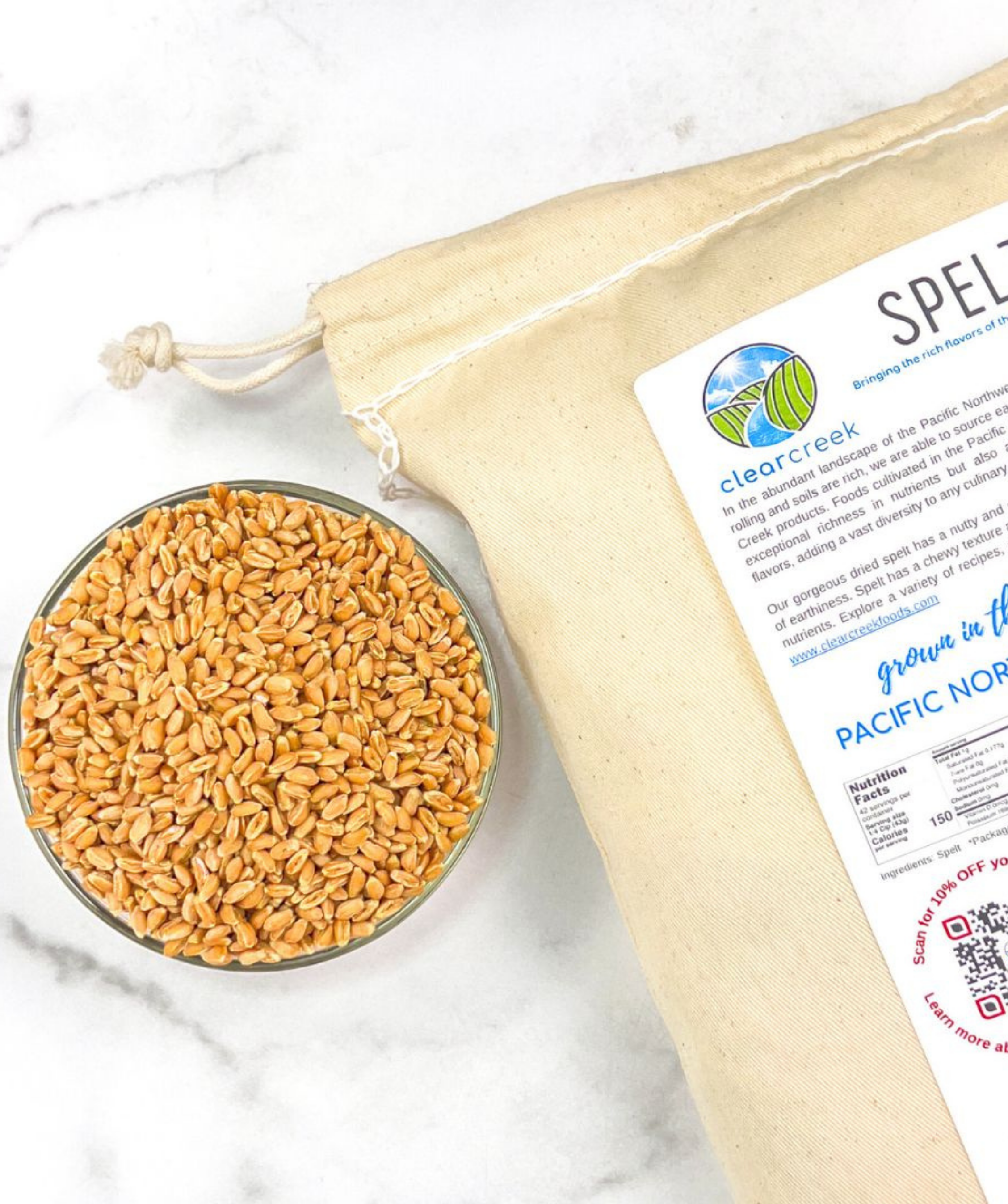 Clear Creek Spelt canvas bag beside a bowl of spelt berries on a marble surface