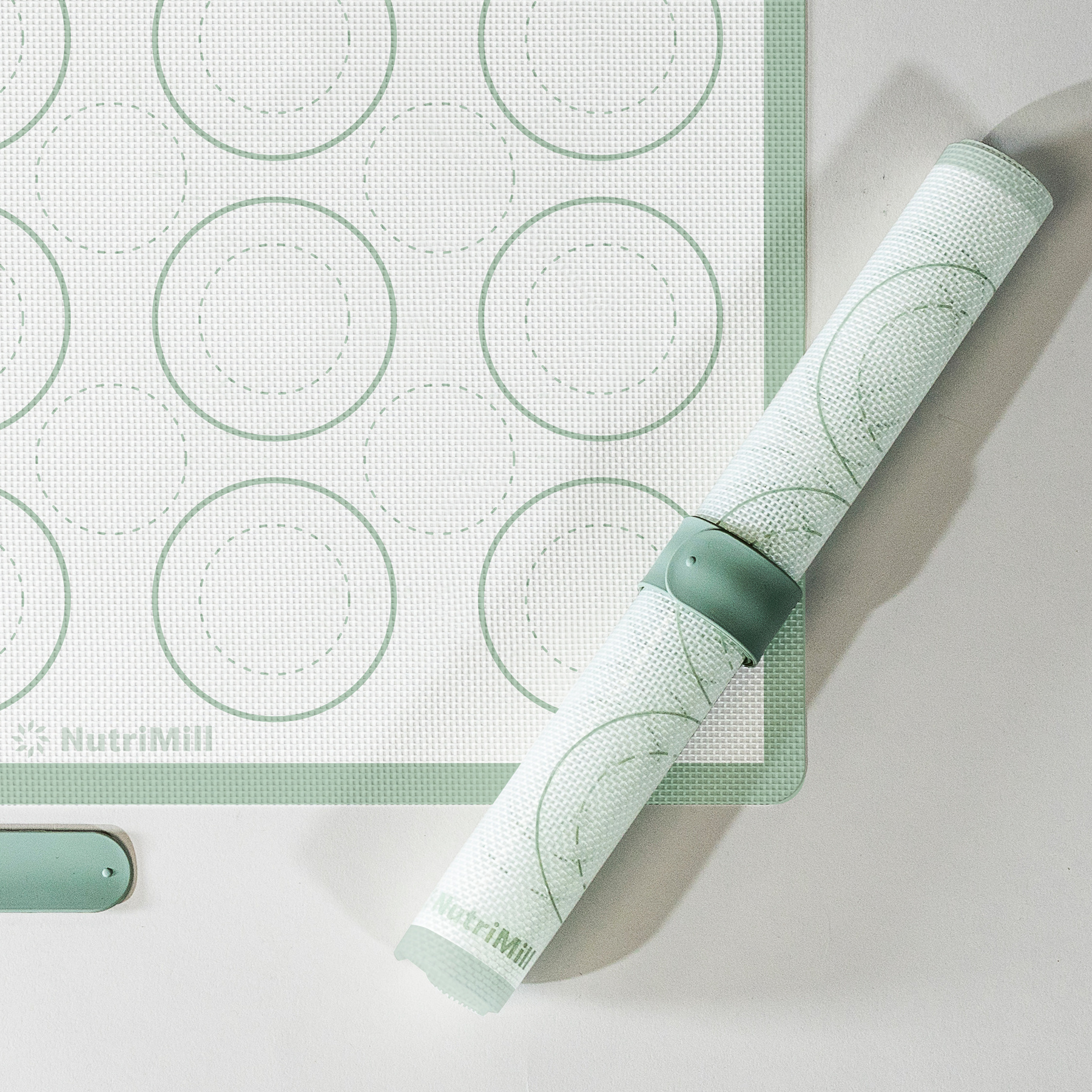 Close-up of a NutriMill green silicone baking mat with macaron circle guides next to a rolled mat
