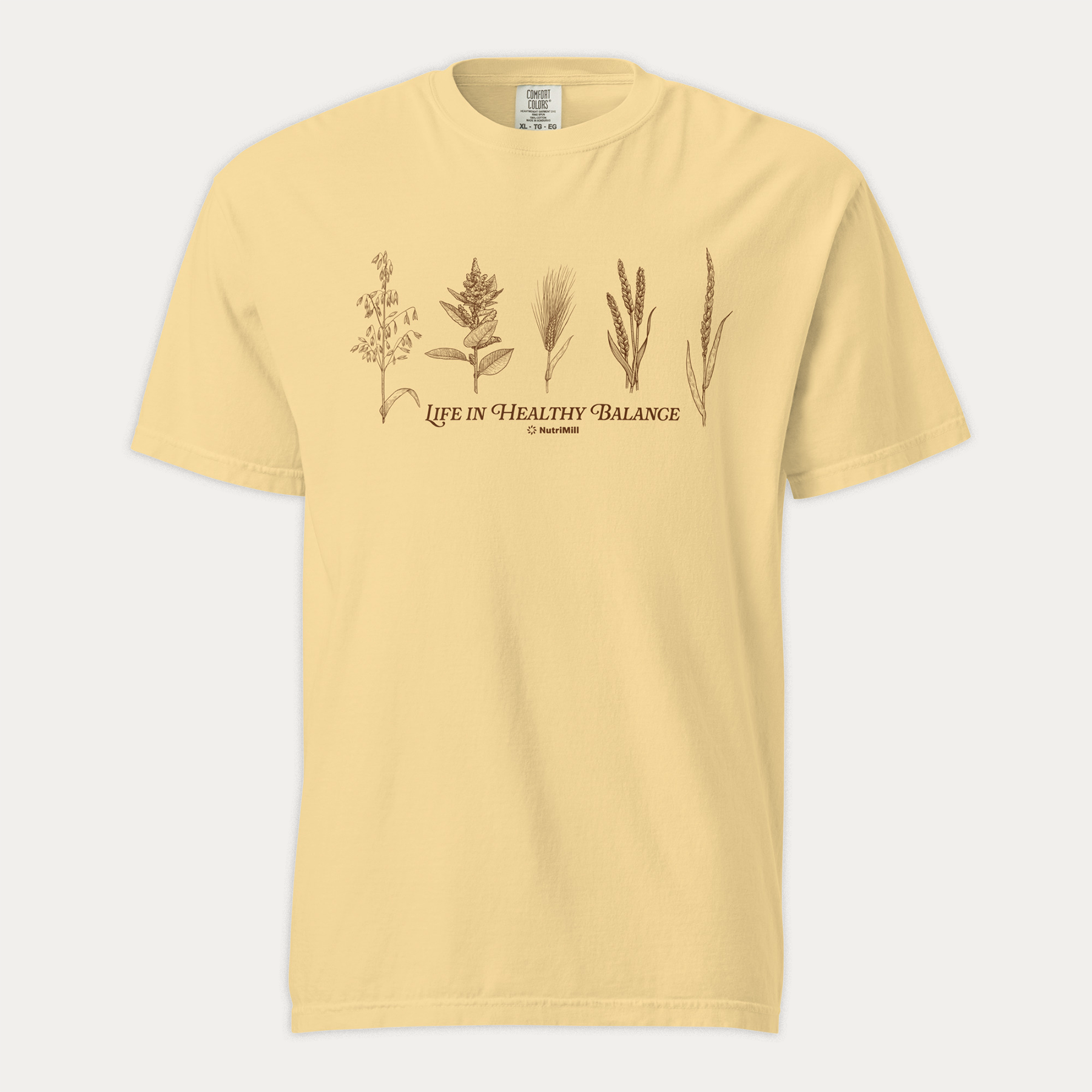 Front view of a butter yellow NutriMill 'Life in Healthy Balance' unisex garment-dyed heavyweight t-shirt with brown wheat and grain illustrations