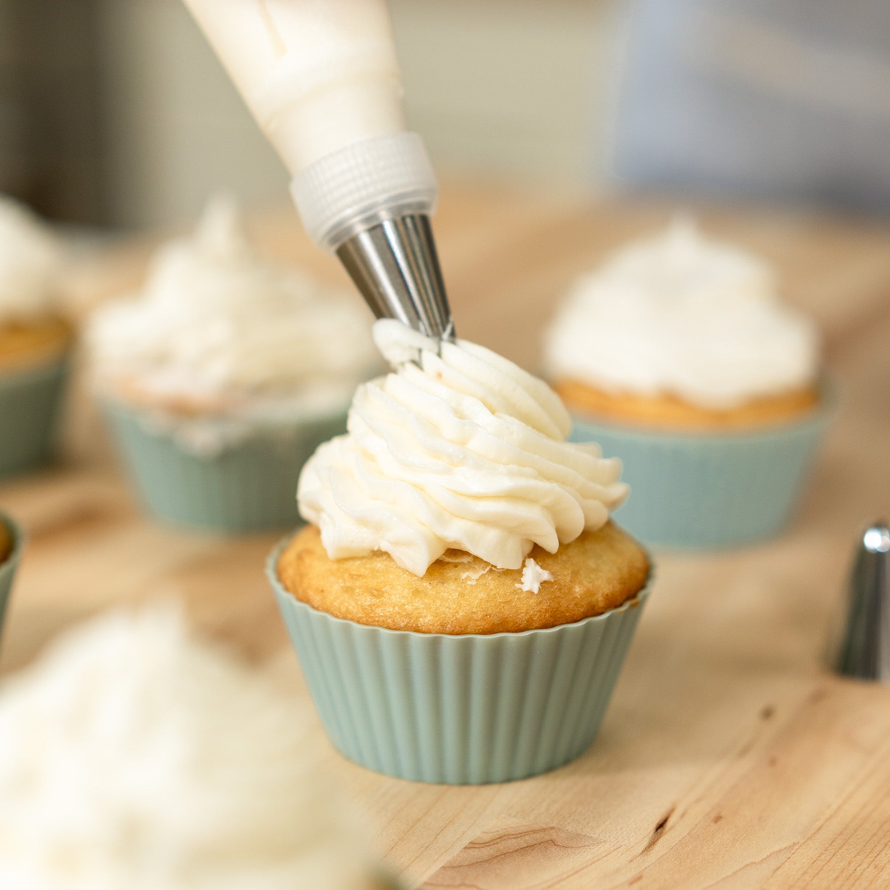 Person icing a cupcake with the NutriMill icing kit on a wooden counter with more cupcakes in the background