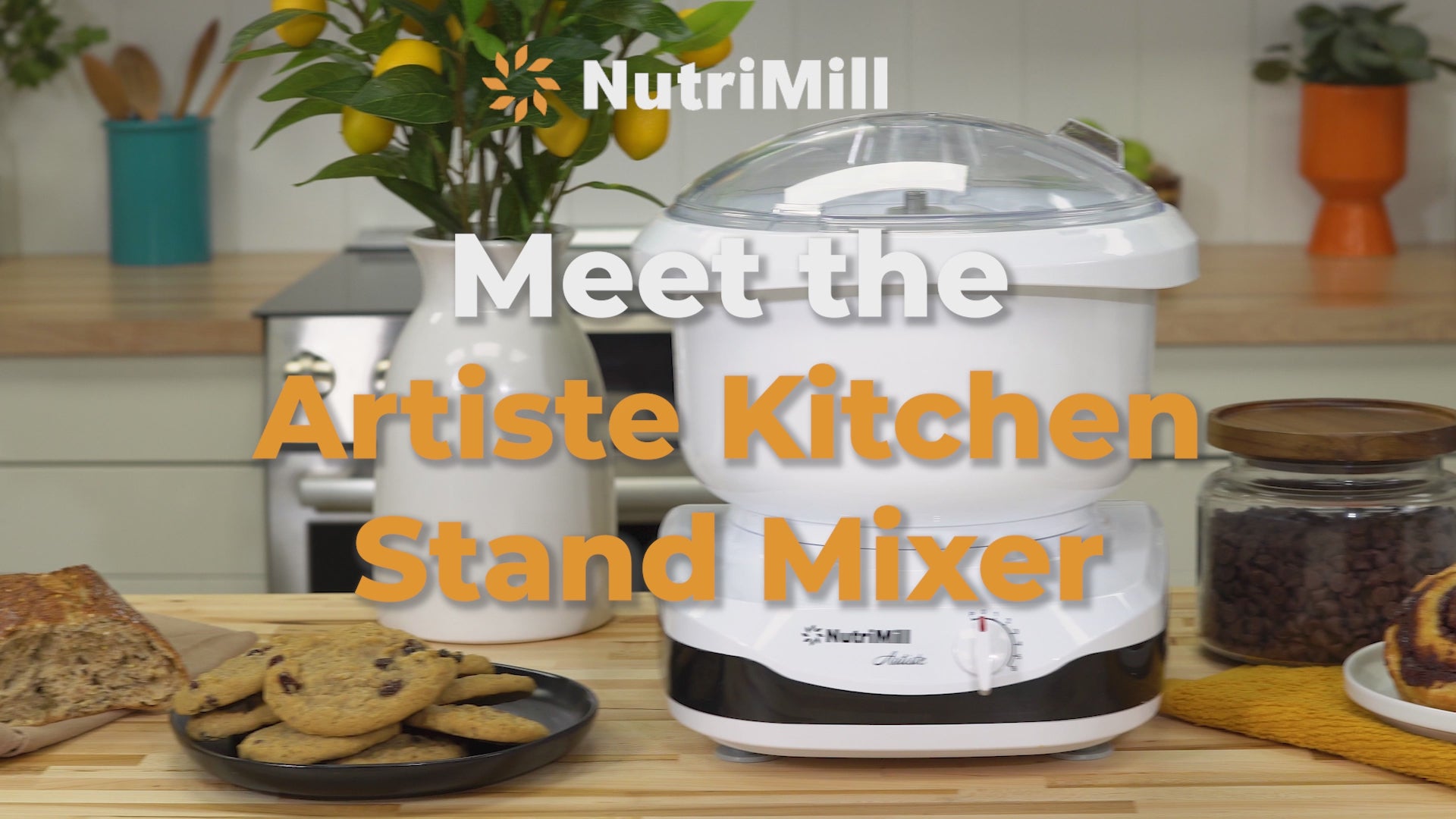 Landscape promotional video introducing the NutriMill Artiste Kitchen Stand Mixer with chocolate chip cookies, sourdough bread, lemons, and coffee beans on a wooden counter